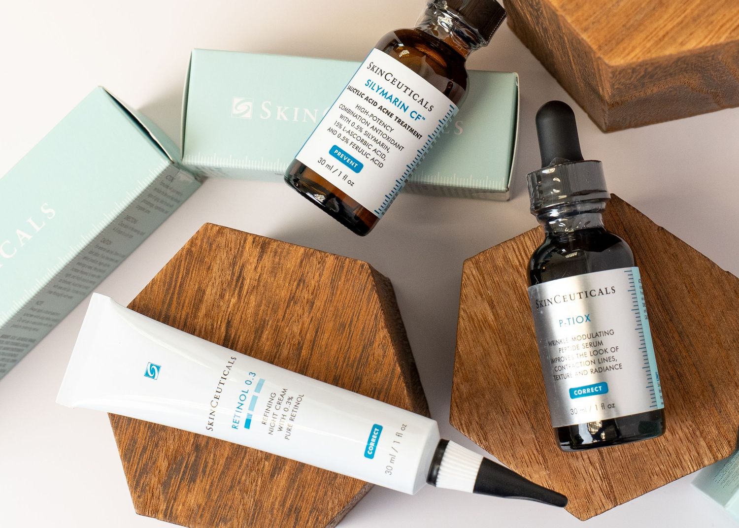 SkinCeuticals skincare products including serums and creams arranged on wooden hexagonal platforms against gray background.