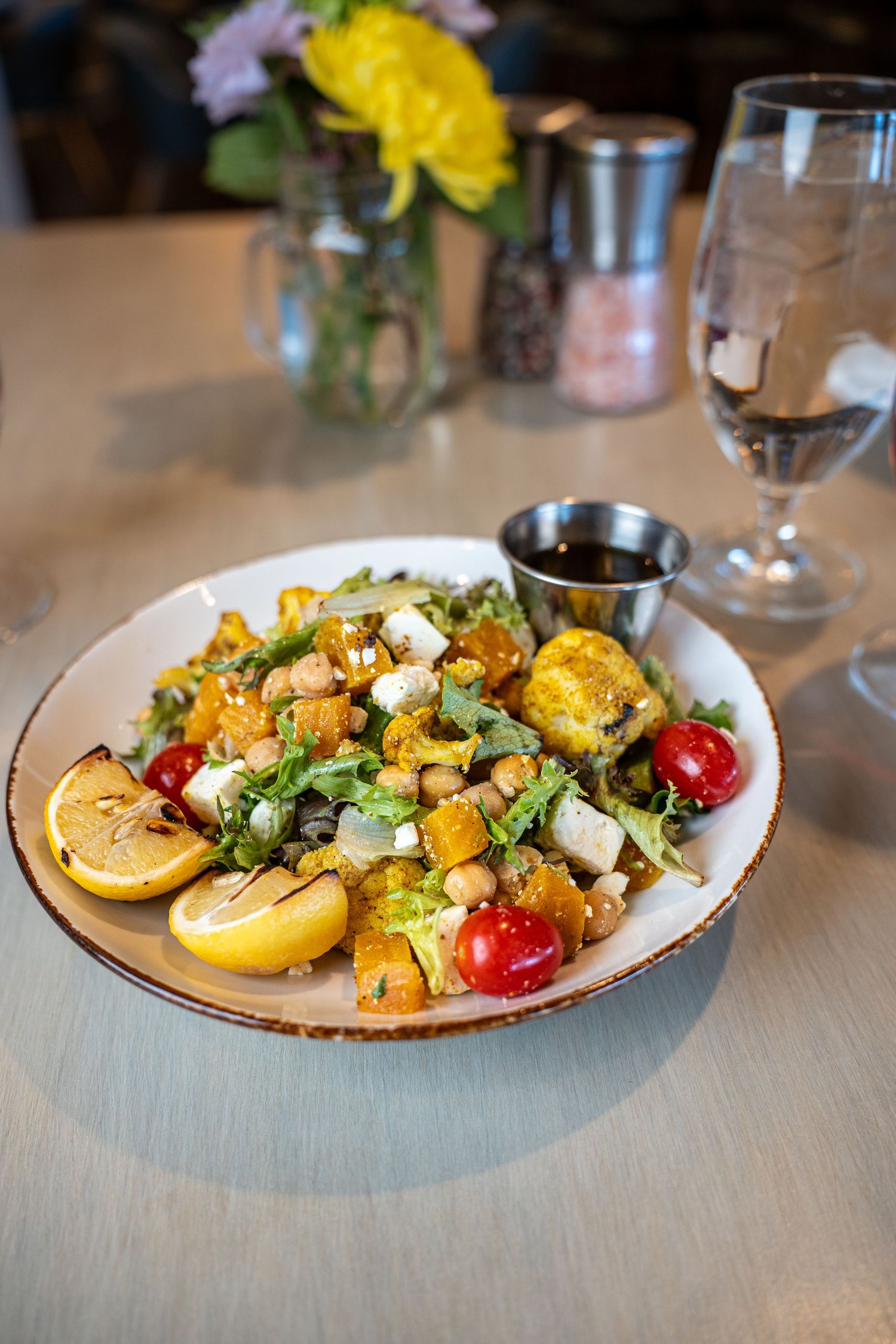 Fresh salad with grilled lemon slices, cherry tomatoes, crumbled cheese and chickpeas on a white plate.