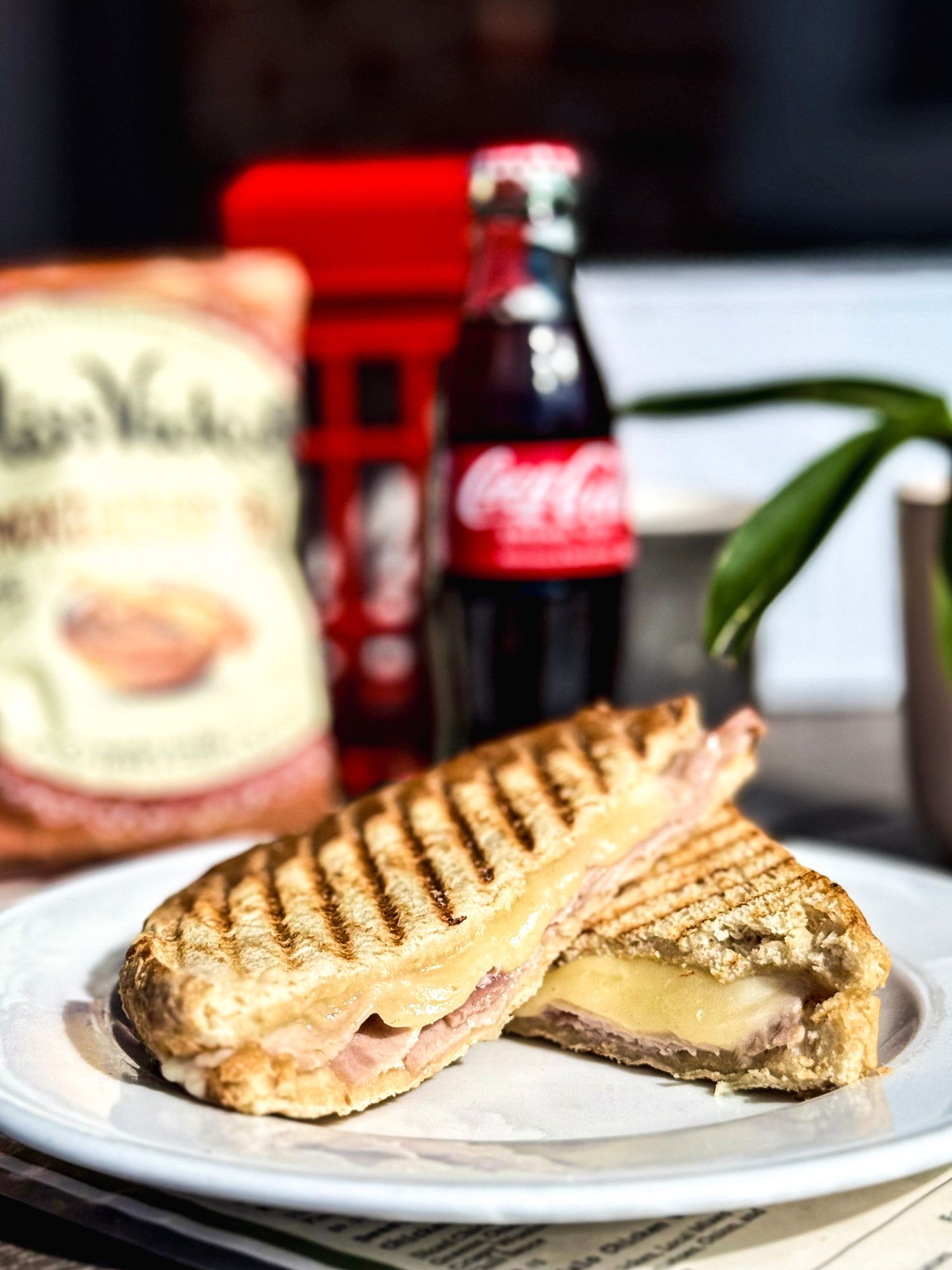 Grilled sandwich with melted cheese on white plate next to a classic Coca-Cola bottle.