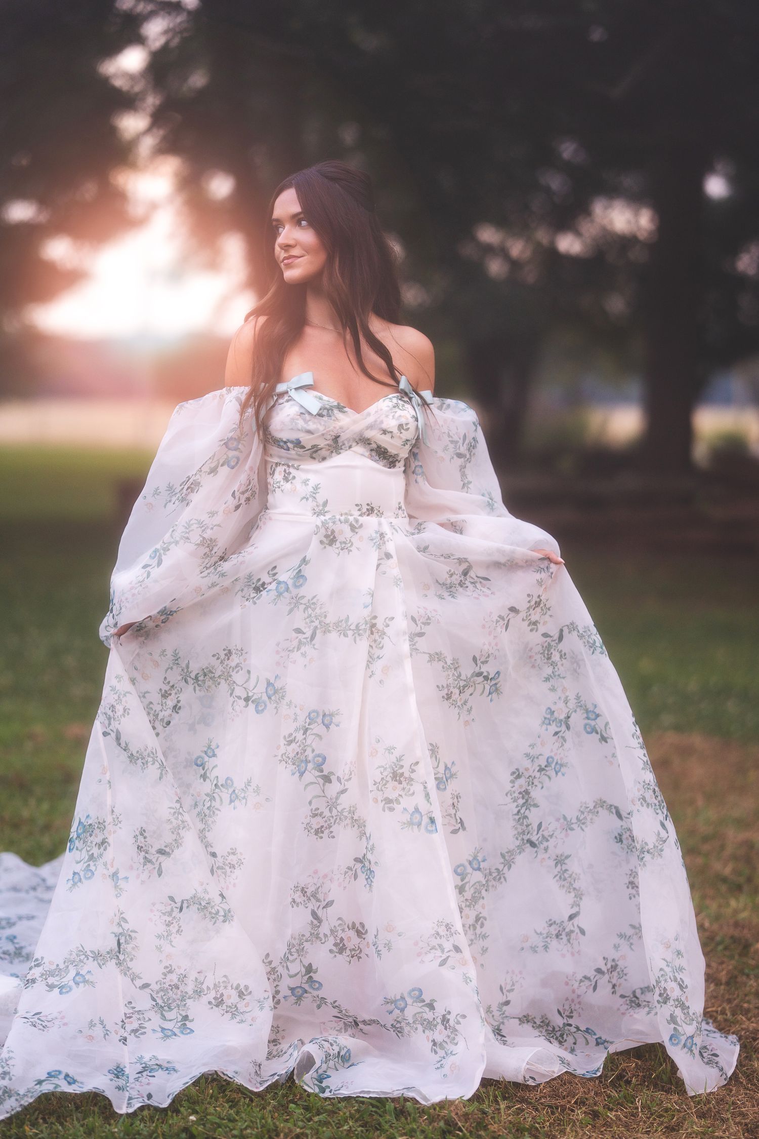 Flowing white lace dress with delicate floral patterns captured in outdoor sunlit setting during romantic photoshoot.