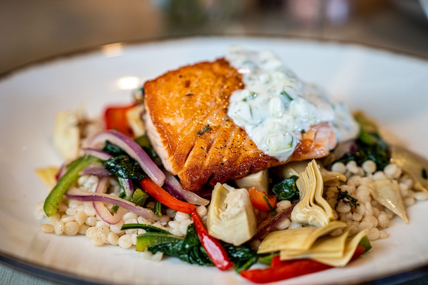 Grilled salmon with creamy sauce served over pasta and vegetables on a white plate.