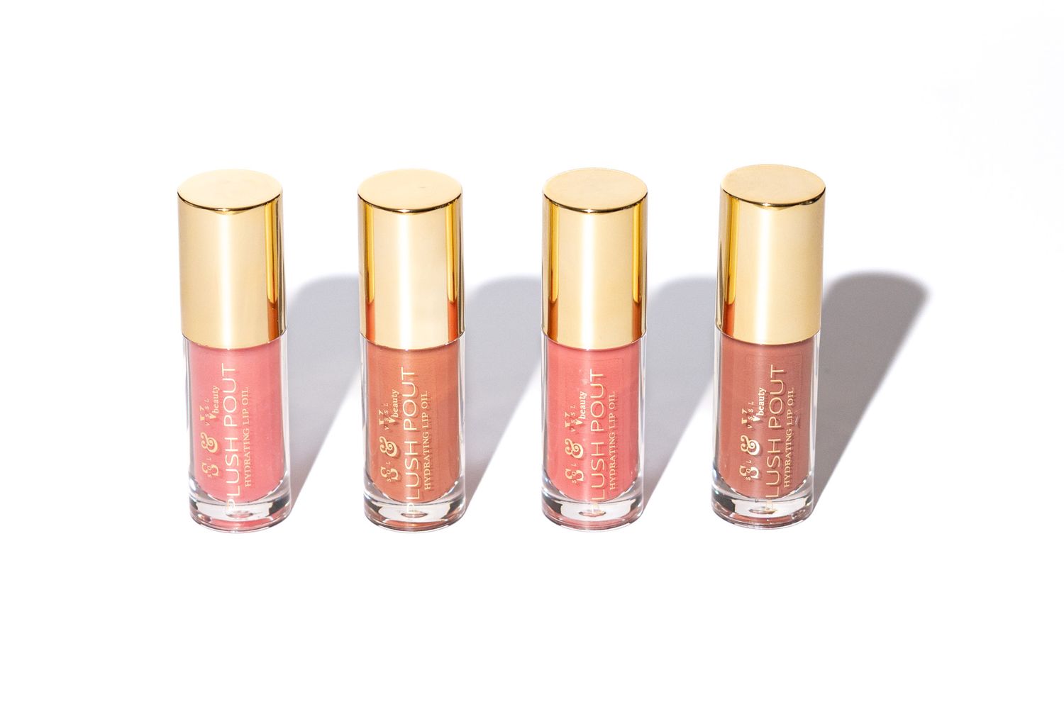 Four pink-toned liquid lipsticks with gold caps lined up in a row casting shadows against a white background.