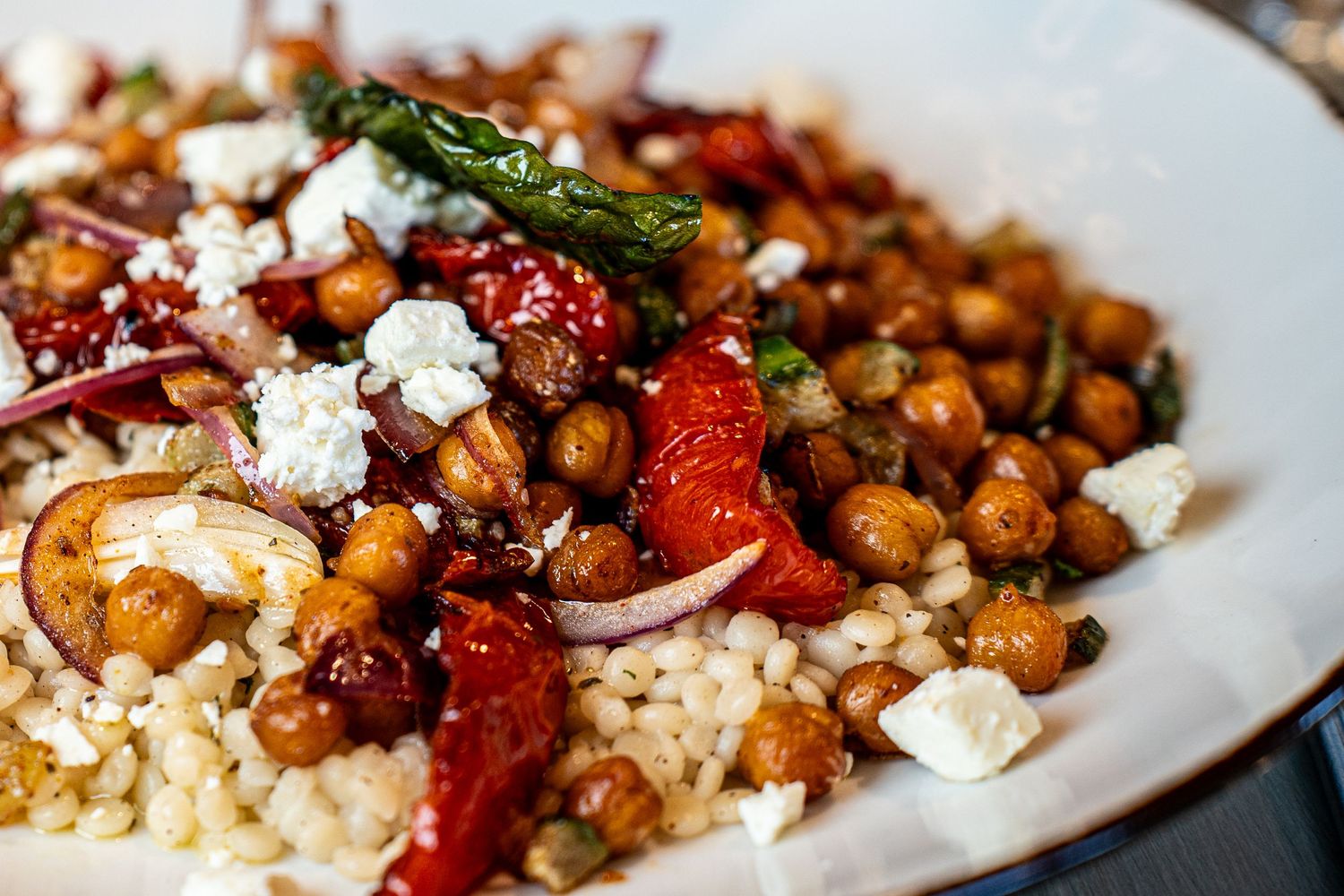 Mediterranean bowl with roasted chickpeas, feta cheese, and grilled vegetables over couscous.