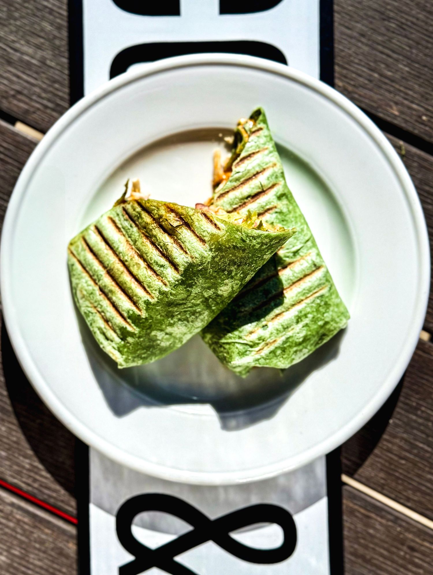 Grilled green wrap sandwich cut in half and served on a white plate with geometric placemat.