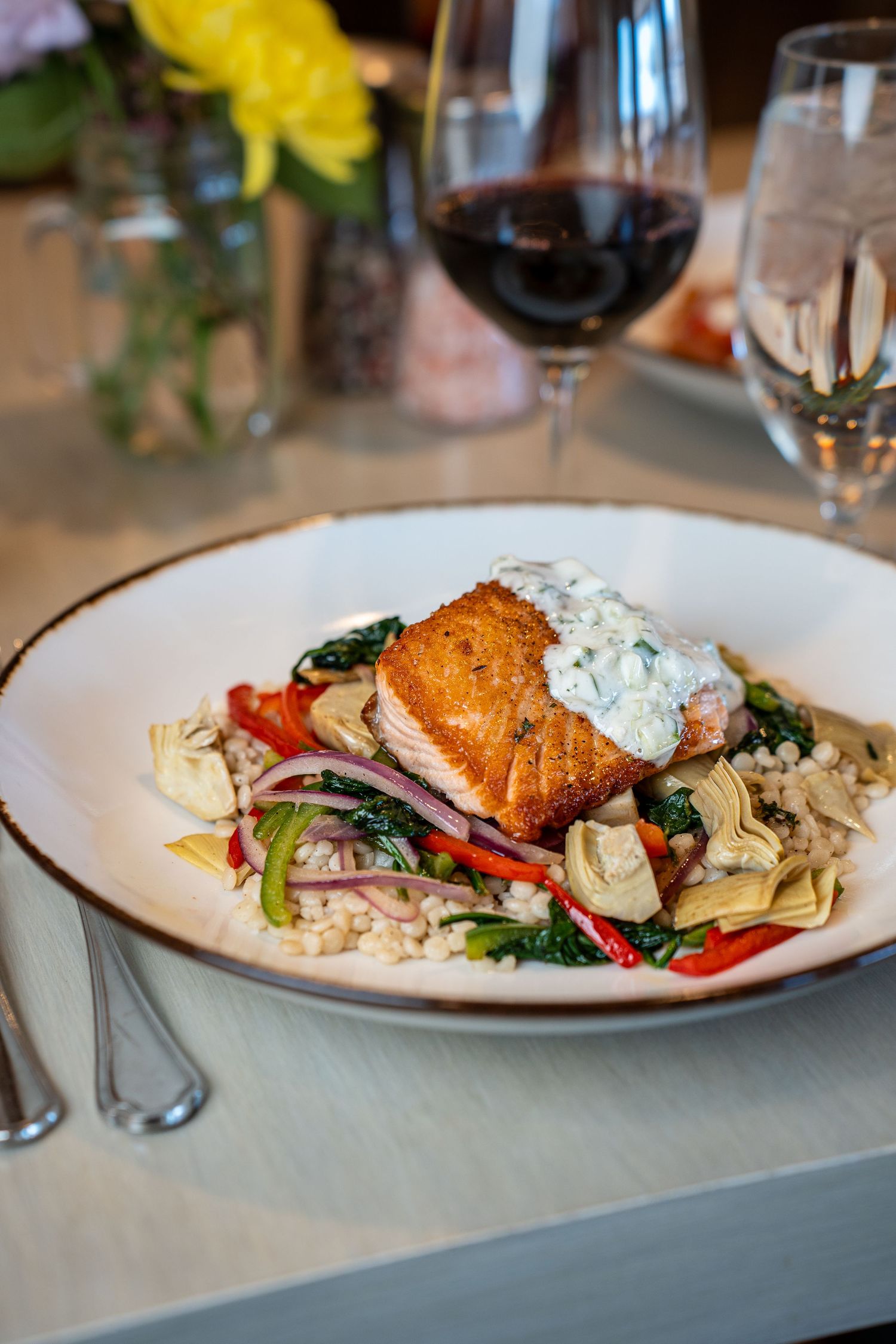 Grilled salmon fillet served with fresh vegetables and creamy sauce on a white plate in an upscale restaurant setting.