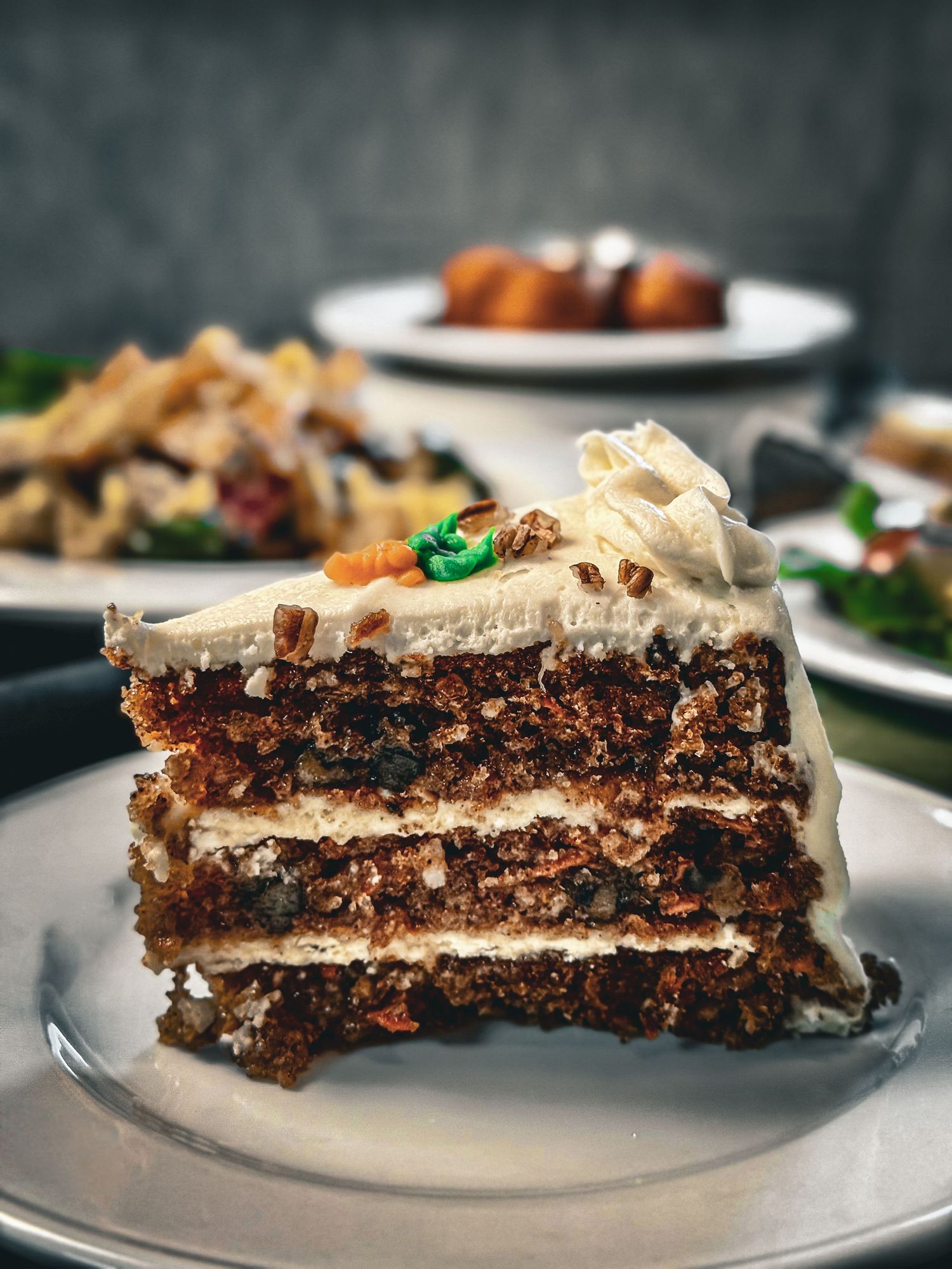 Close-up of a layered chocolate cake slice with creamy frosting and nuts on top.