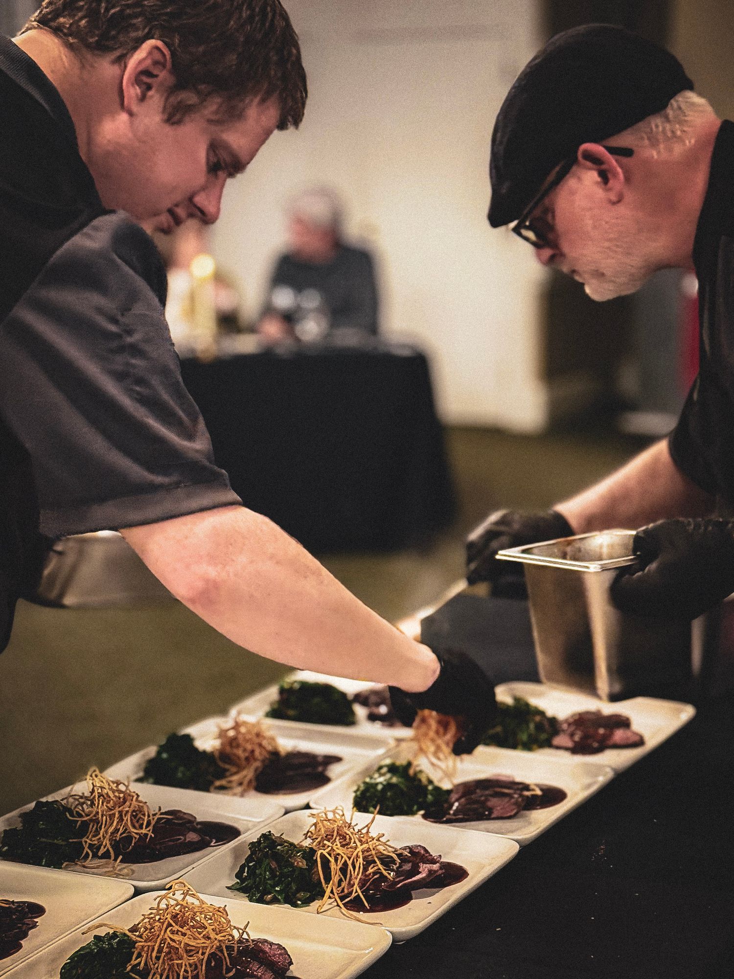 Chefs plating elegant dishes with microgreens and garnishes in a restaurant kitchen.