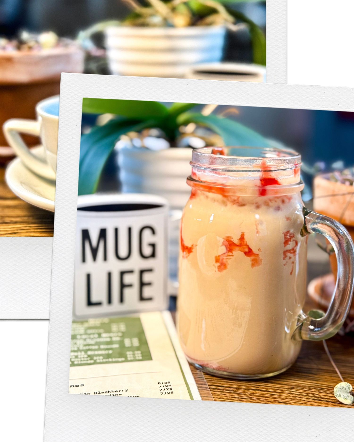 Pink smoothie in mason jar next to Mug Life sign on wooden table.