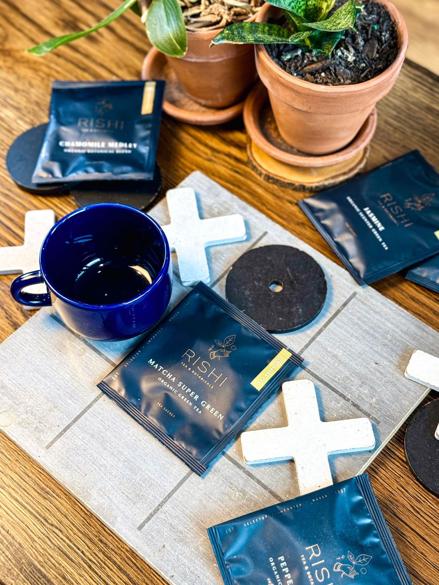 Blue ceramic mug with coffee sachets and potted plants on wooden table setting.