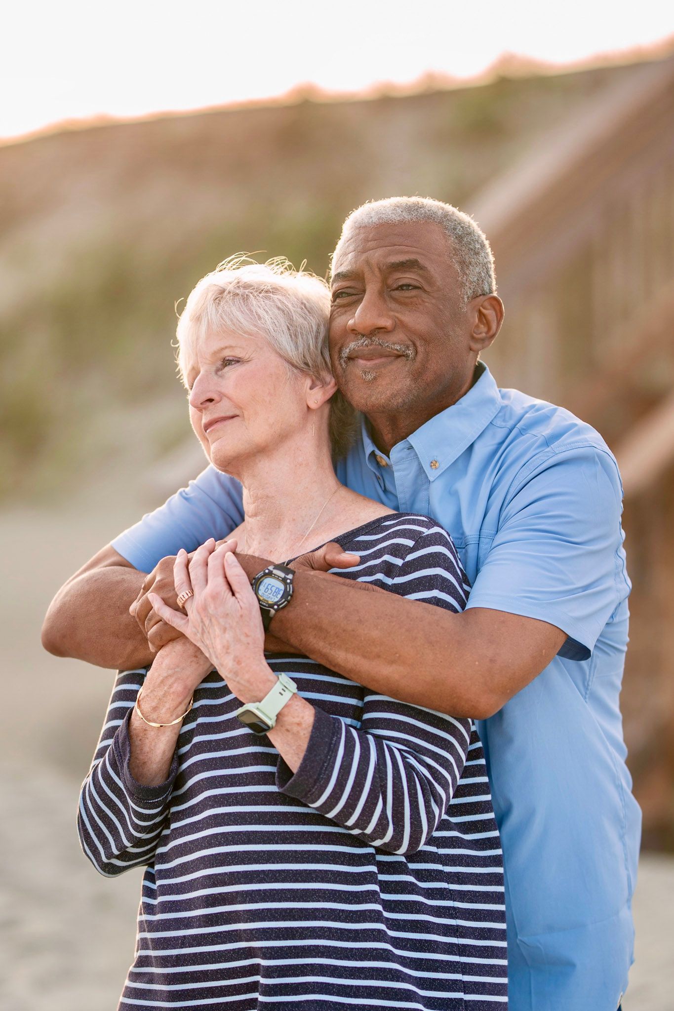 Happy mature couple embracing on beach during golden hour sunset.