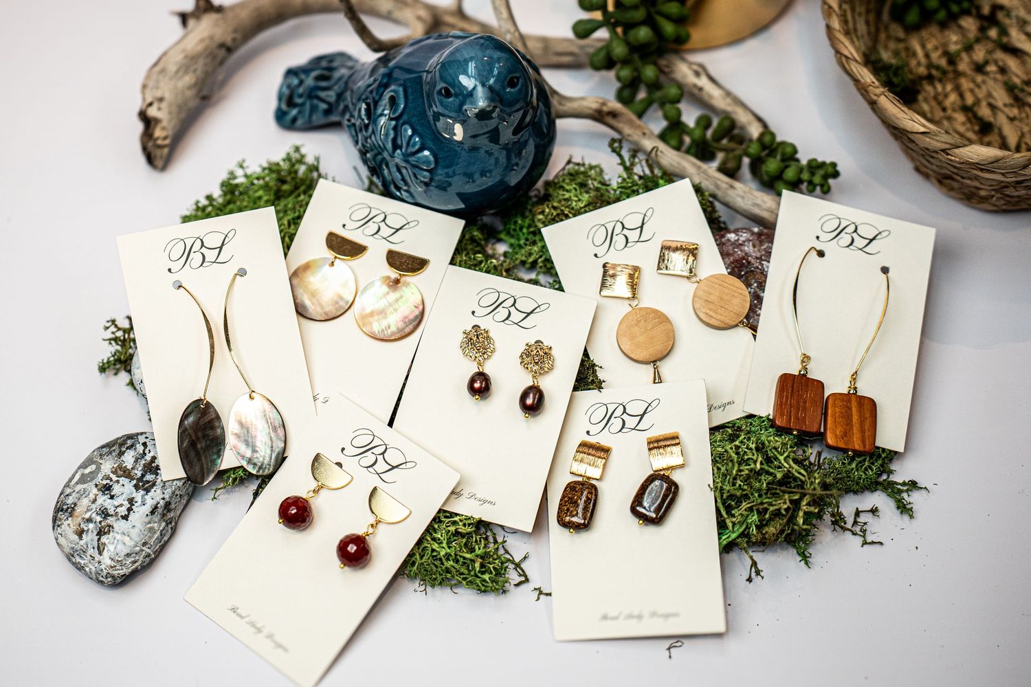 Multiple pairs of handmade earrings displayed with crystals and natural elements on white cards.