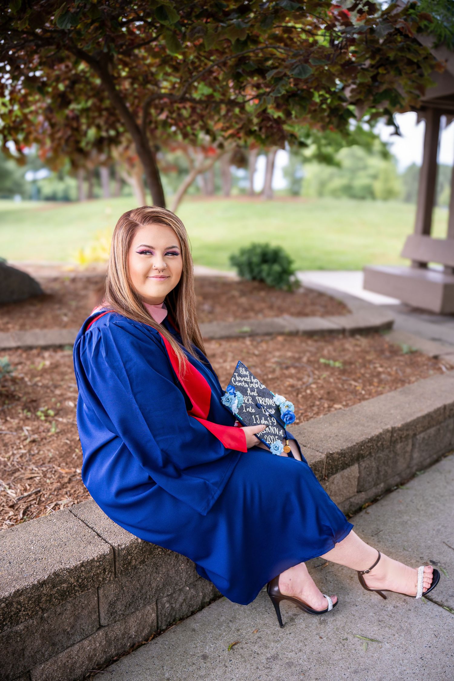 A person in bright blue graduation gown and red scarf sits on concrete steps in an outdoor setting.