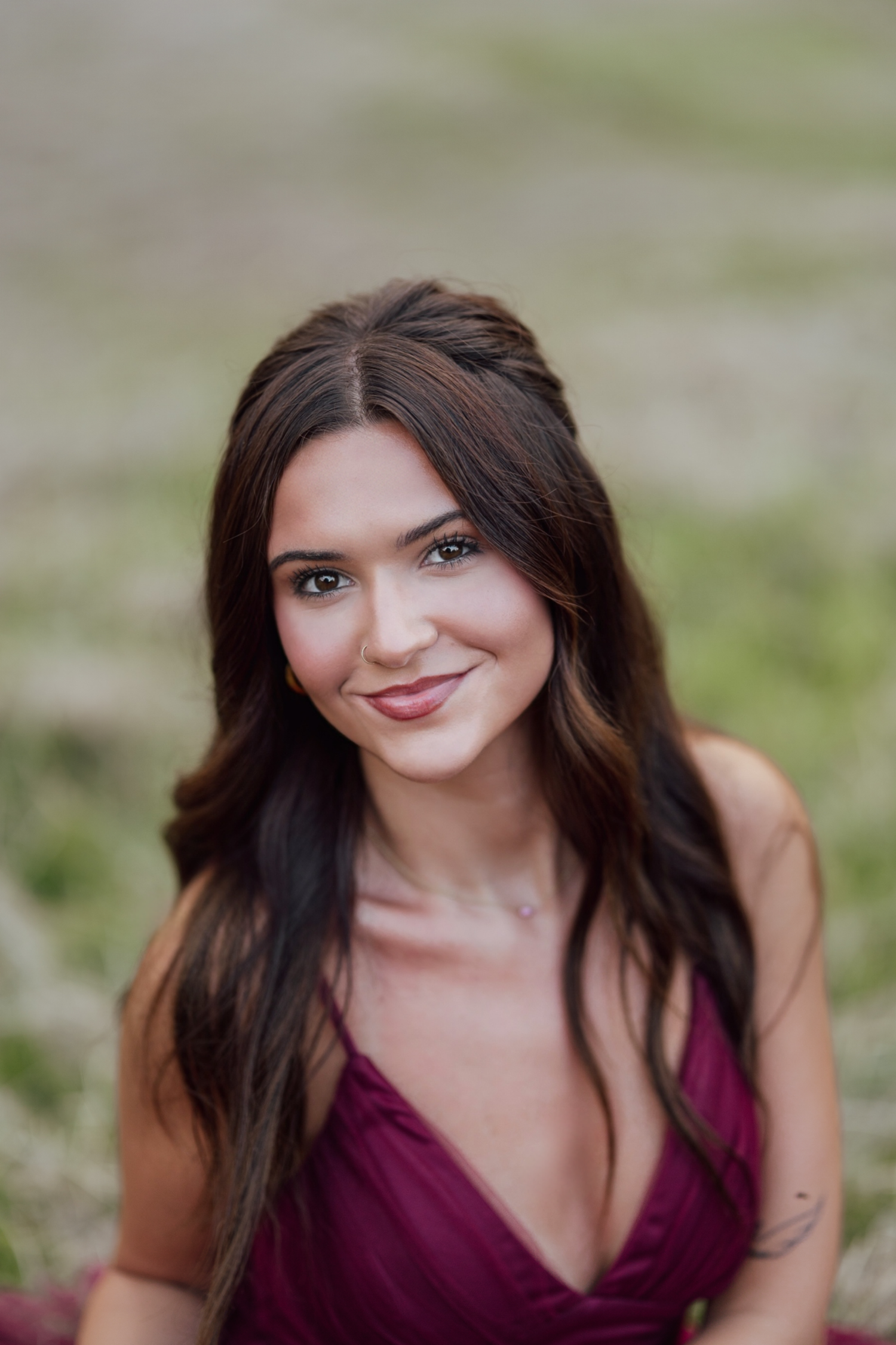 Close-up outdoor portrait of woman with long dark hair wearing a burgundy top smiling at the camera.
