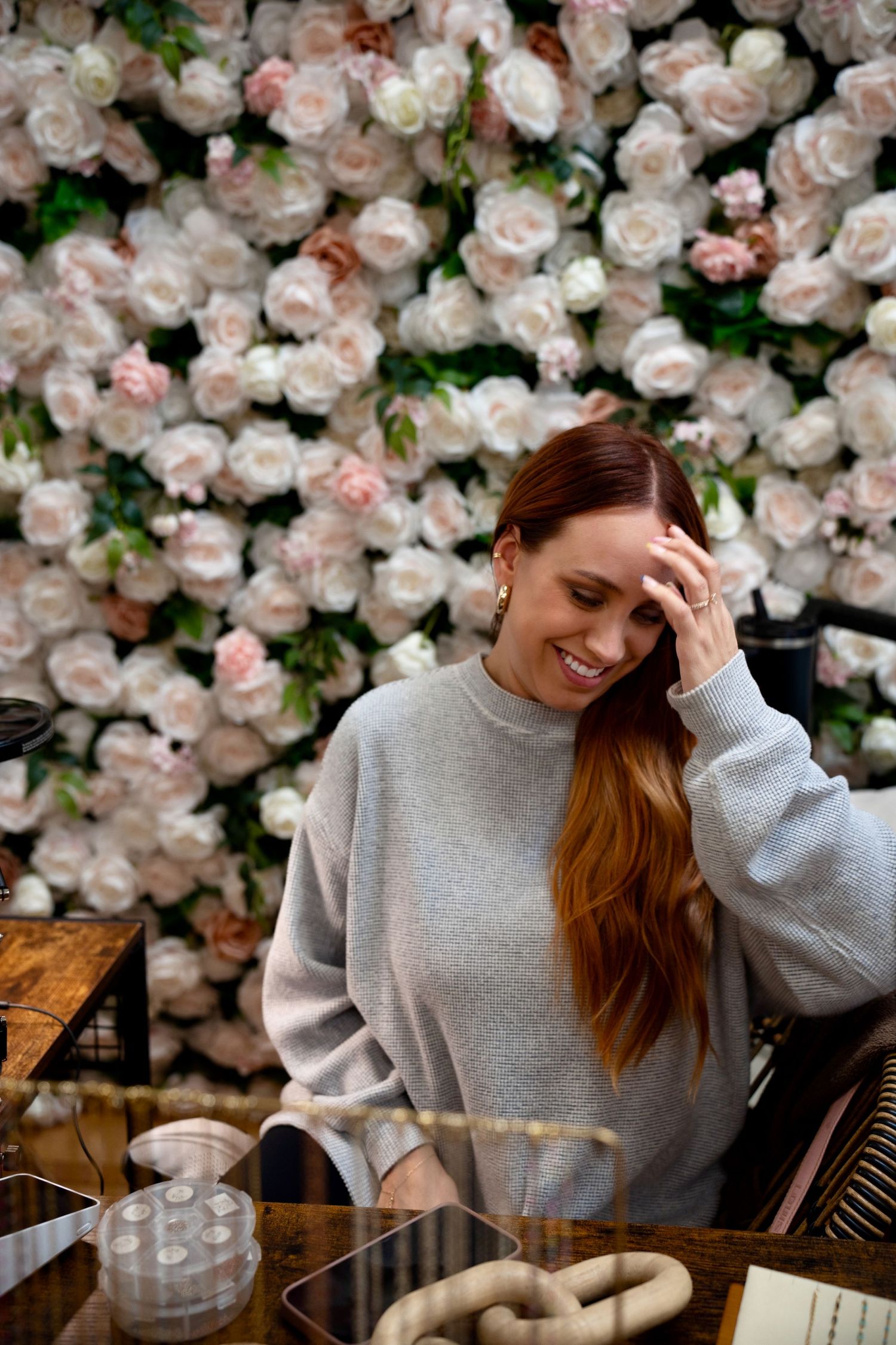 A cozy scene with a person in gray sweater near a wall of pink roses at a cafe table.