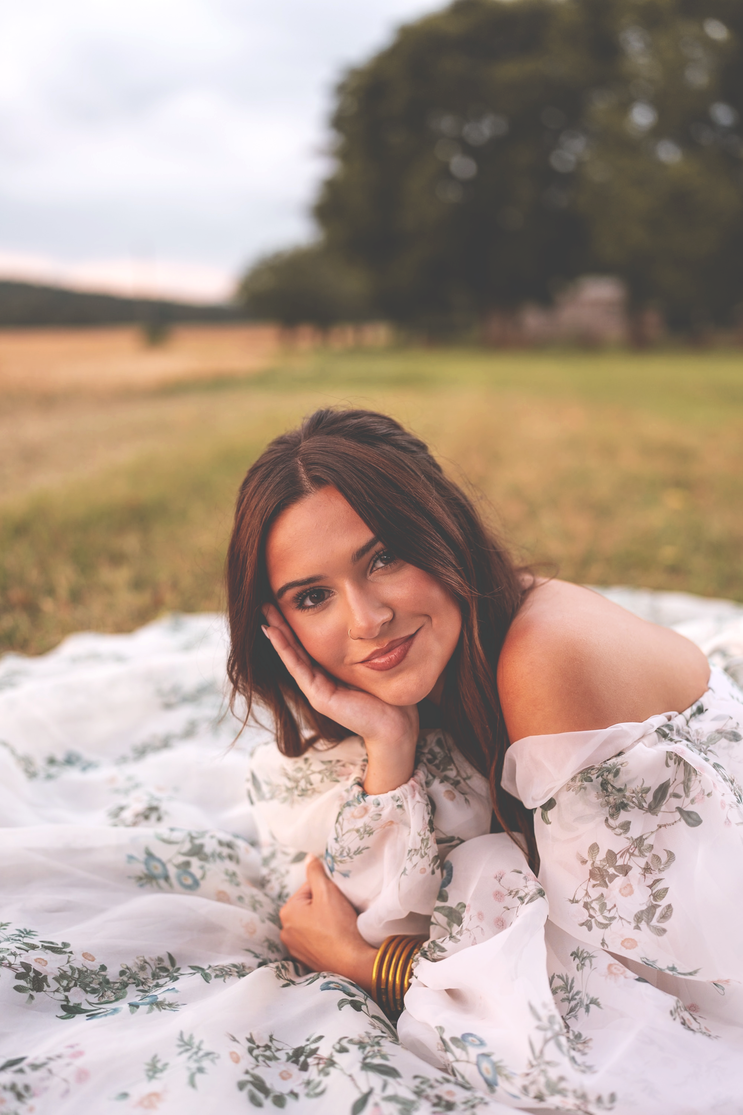 Young woman in delicate white dress with floral details poses gracefully in outdoor nature setting.