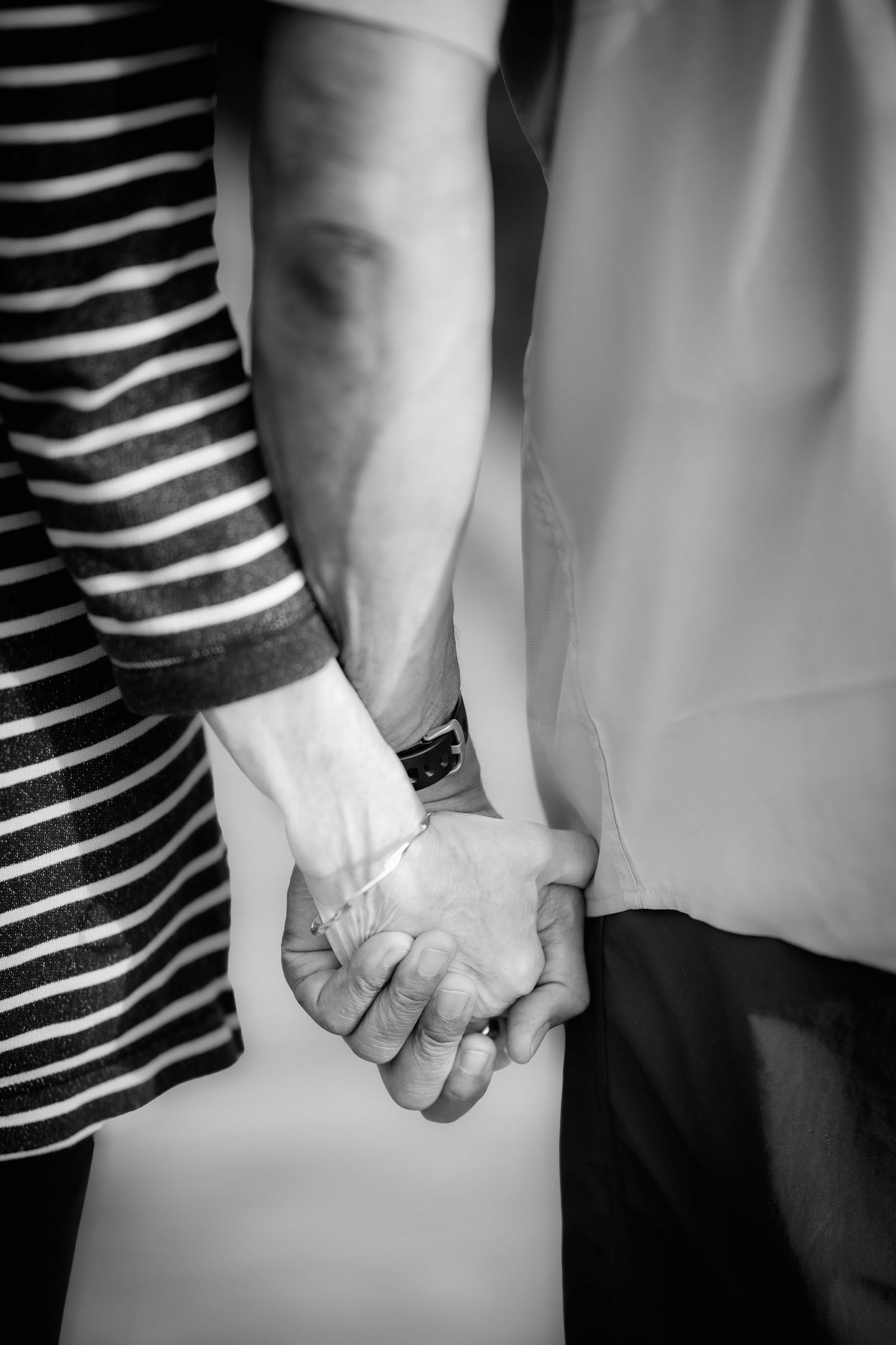 Close-up black and white photo of two people holding hands, with one wearing a striped dress and other wearing plain clothing.
