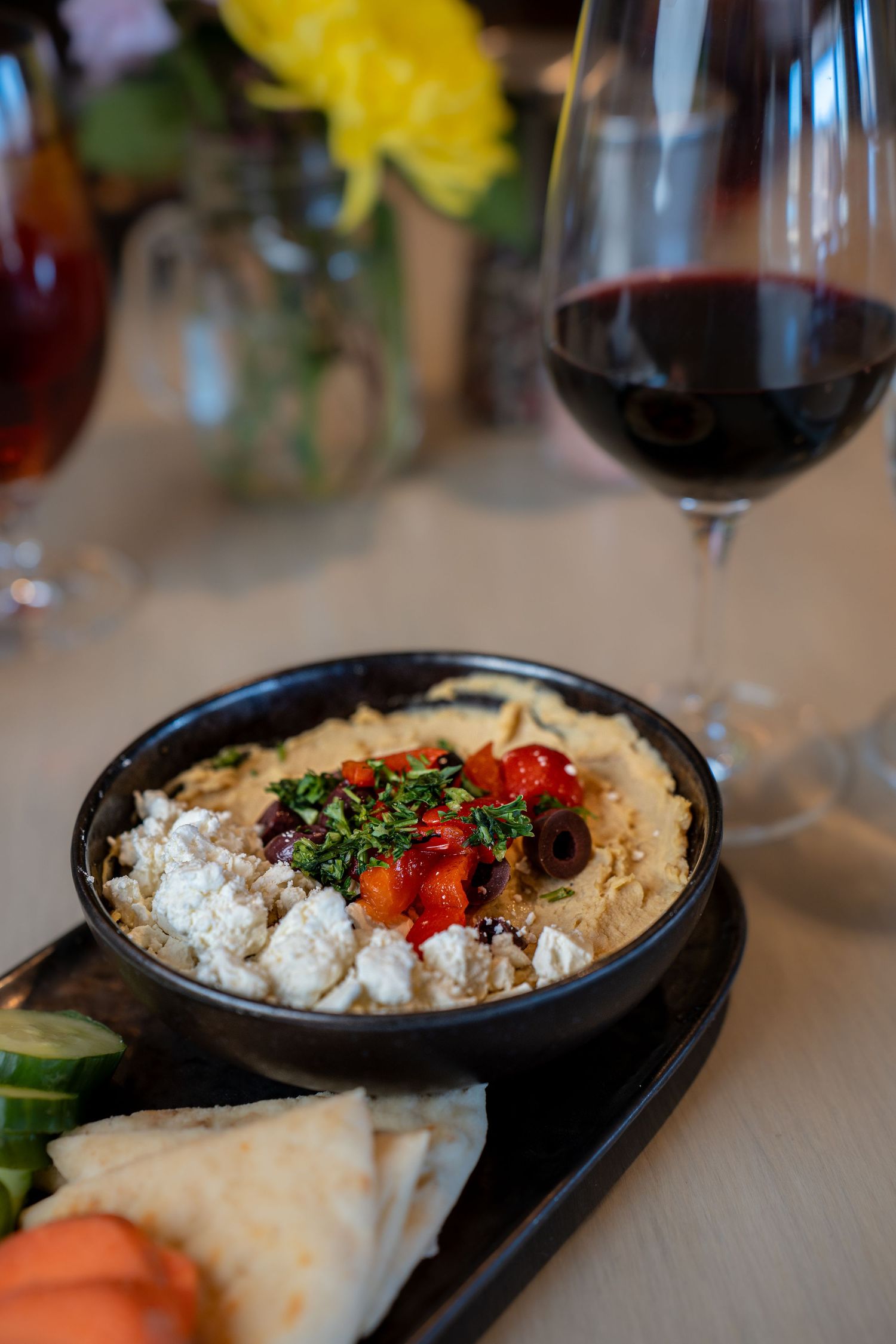Mediterranean dip served with pita bread and vegetables alongside a glass of red wine.