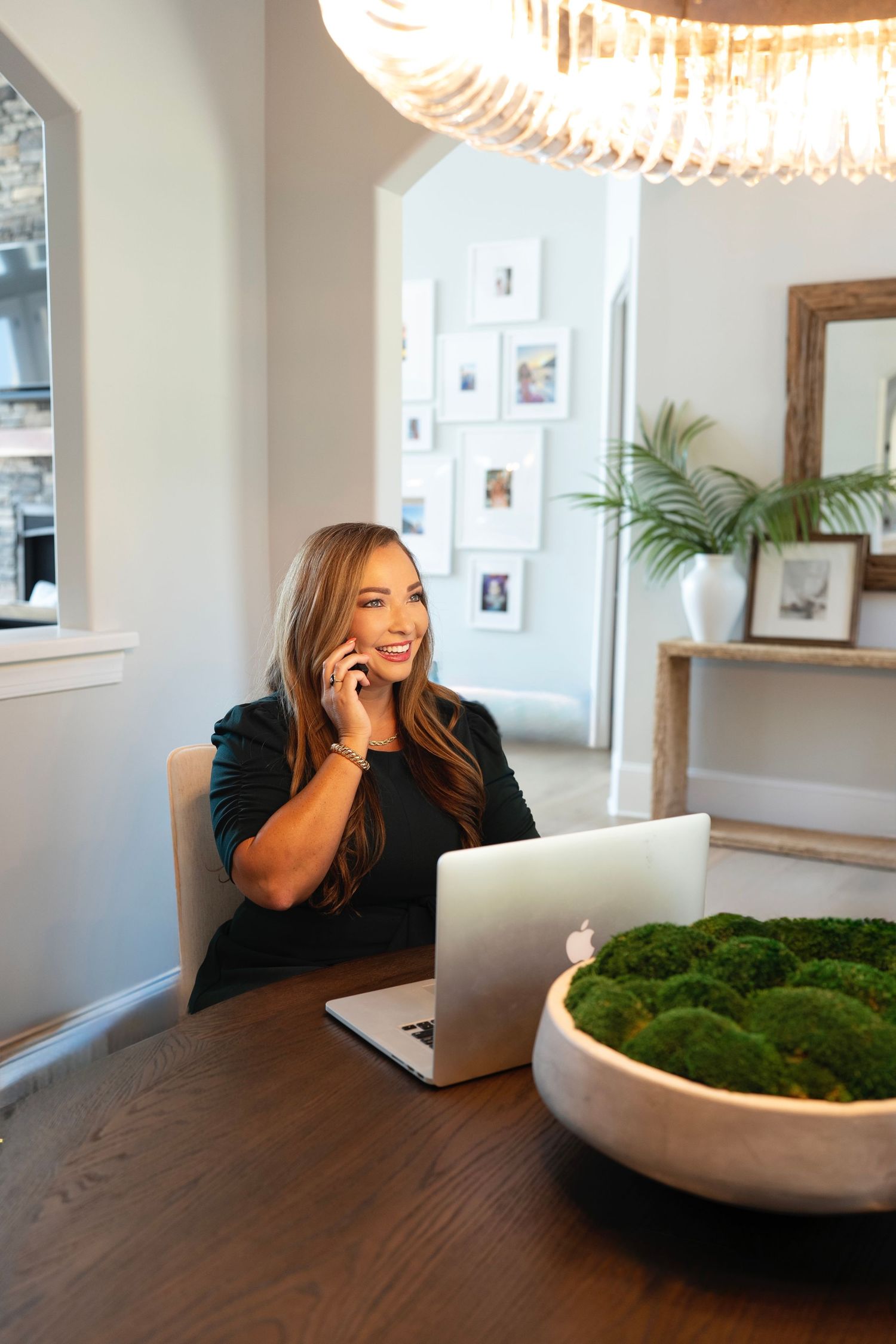 A person working on a laptop and laughing at a modern dining table with a decorative moss bowl centerpiece.