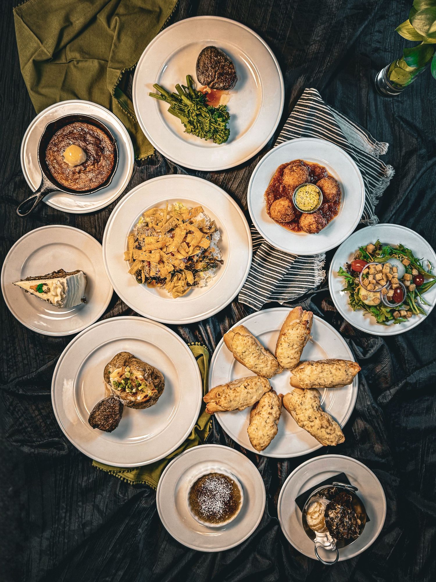 Overhead view of multiple plated dishes including pasta, salads, and appetizers on white plates.