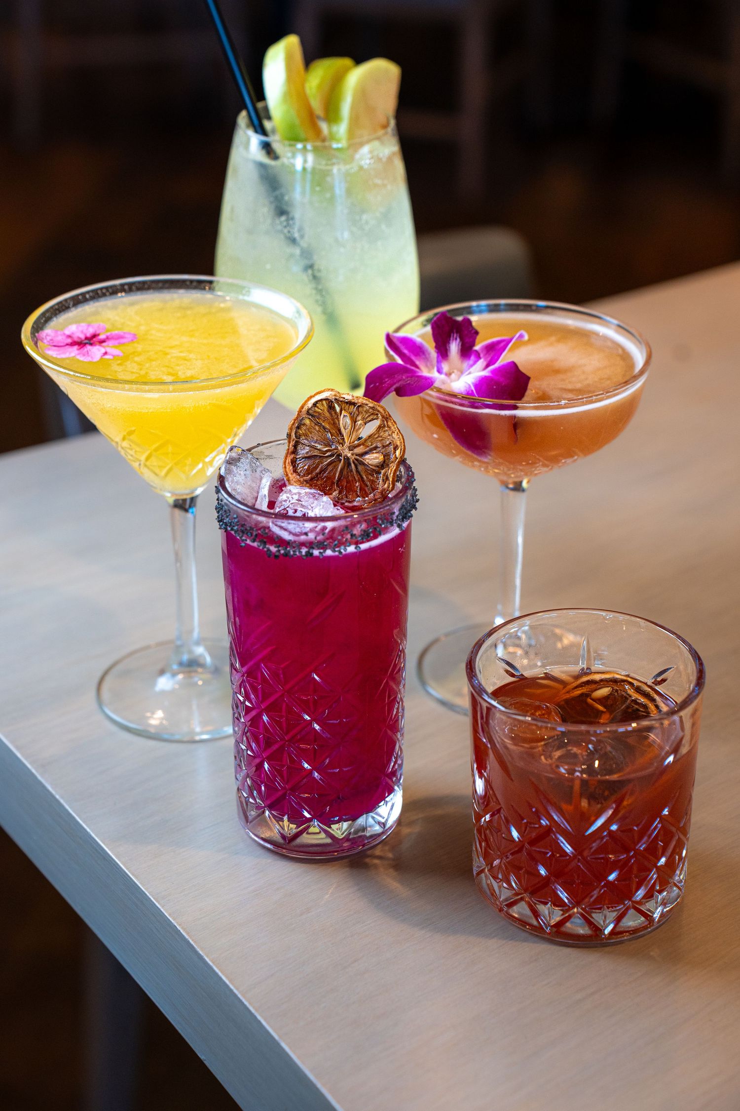 Colorful craft cocktails garnished with fruit and flowers arranged on a bar counter.