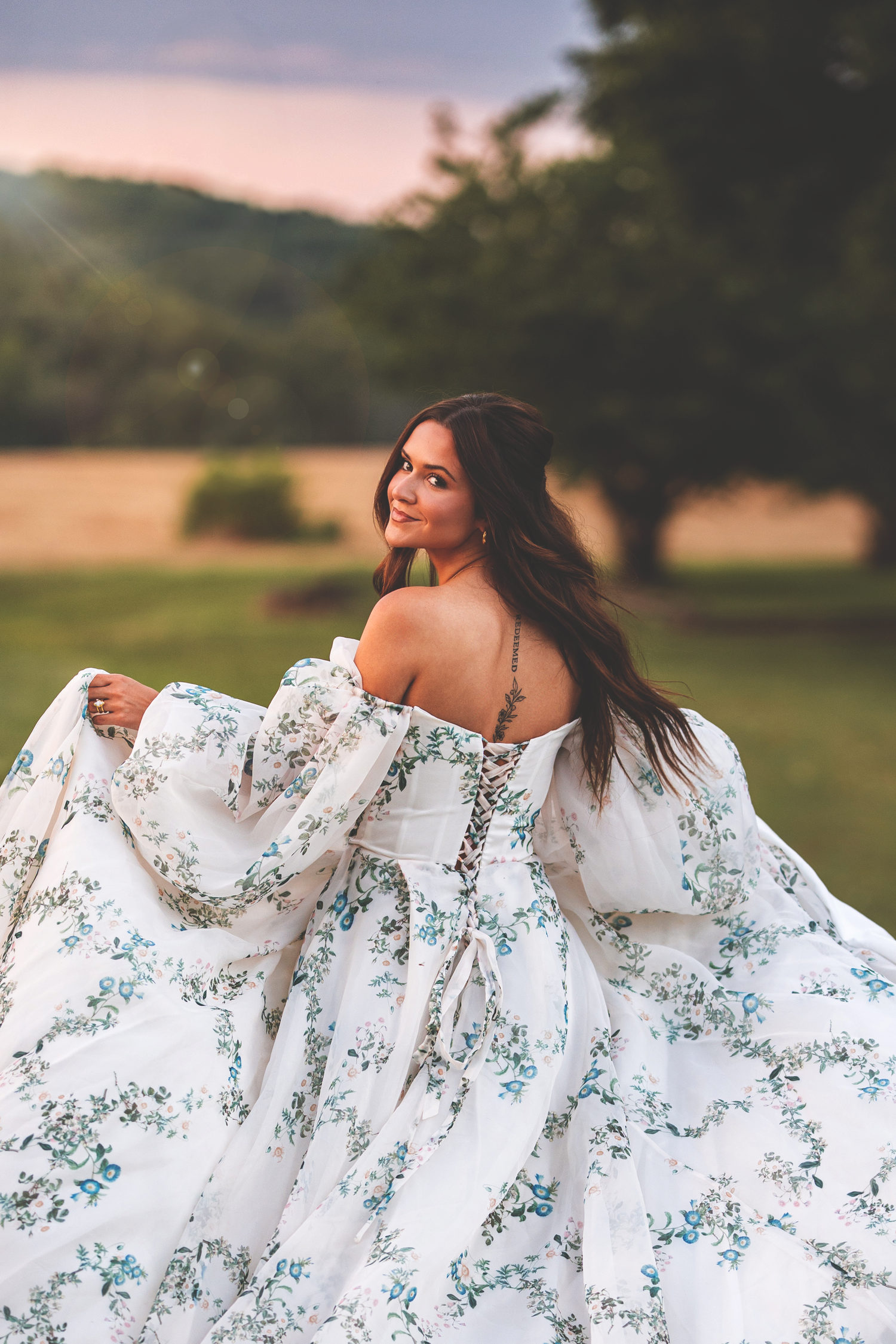 A flowing white dress with blue floral patterns twirls gracefully in a dreamy outdoor sunset setting.