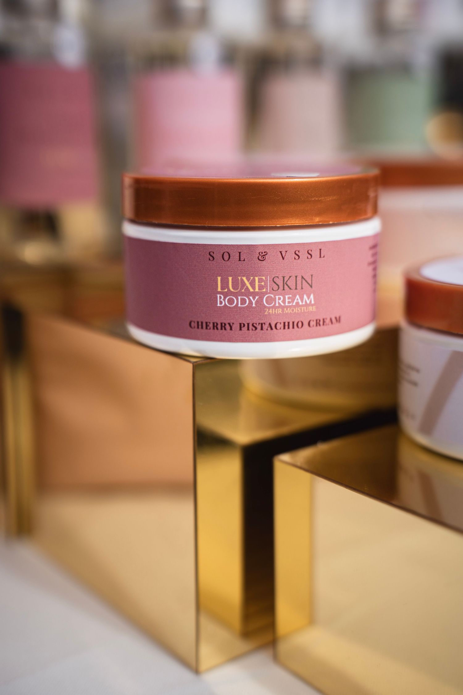Pink luxe skin body cream jar from Sol & VSSL displayed on gold platform.