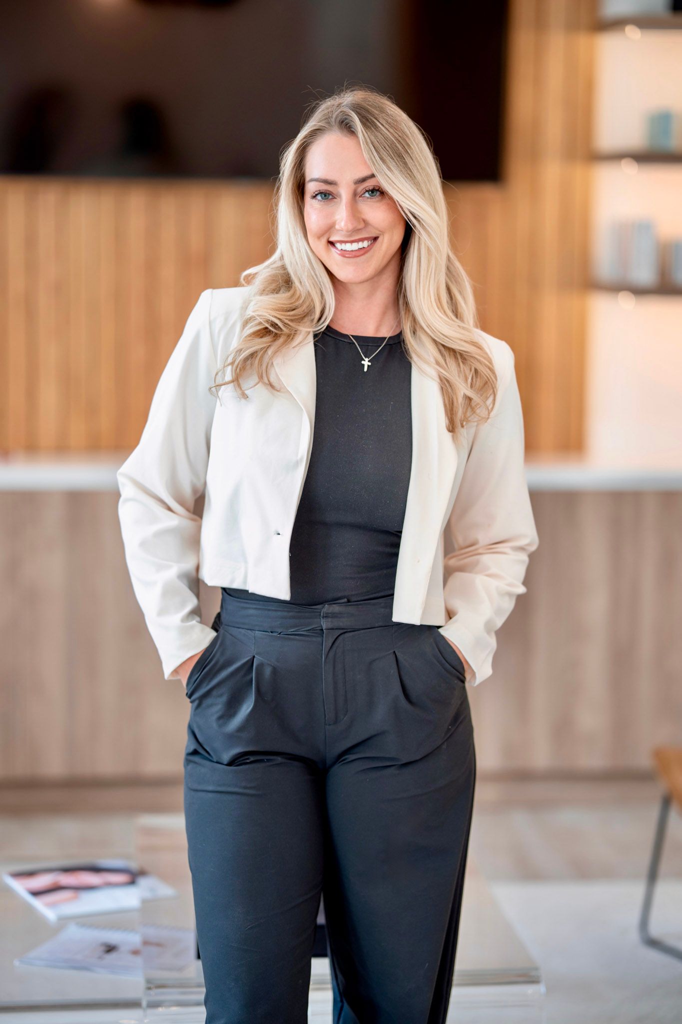 Professional wearing cream blazer and dark pants in modern office setting.