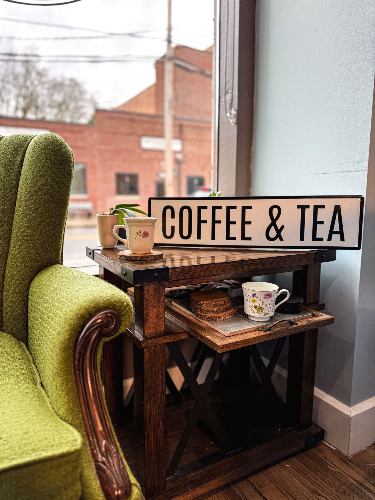 Vintage wooden side table with Coffee & Tea sign next to lime green armchair near window.
