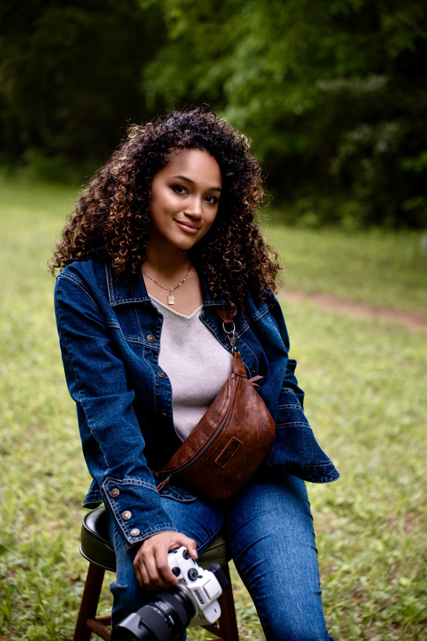 Portrait of photographer with camera and fanny pack sitting outdoors in denim jacket.