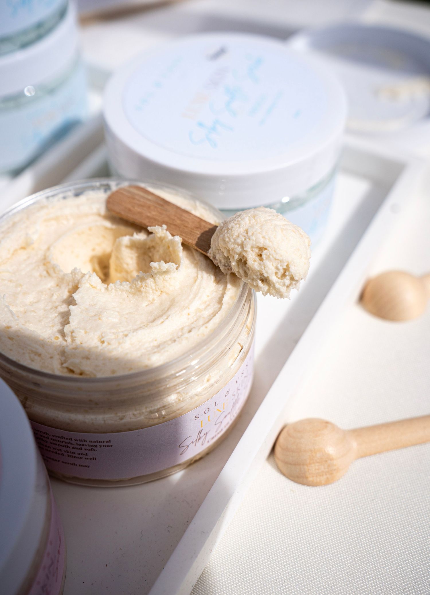Creamy beige-colored body butter product displayed in white containers.