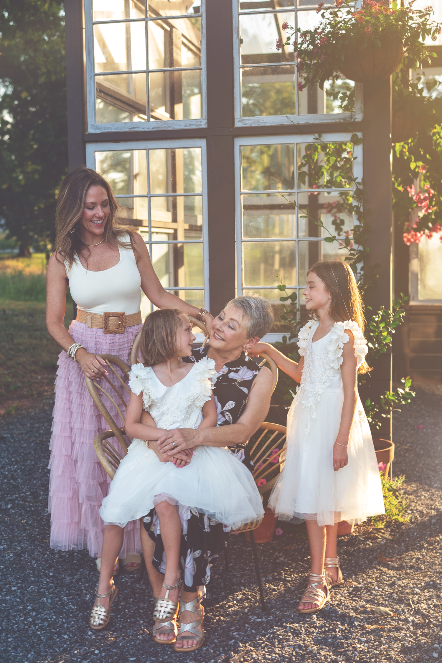 A family shares a joyful moment together outdoors, wearing light colored dresses in the warm sunlight.