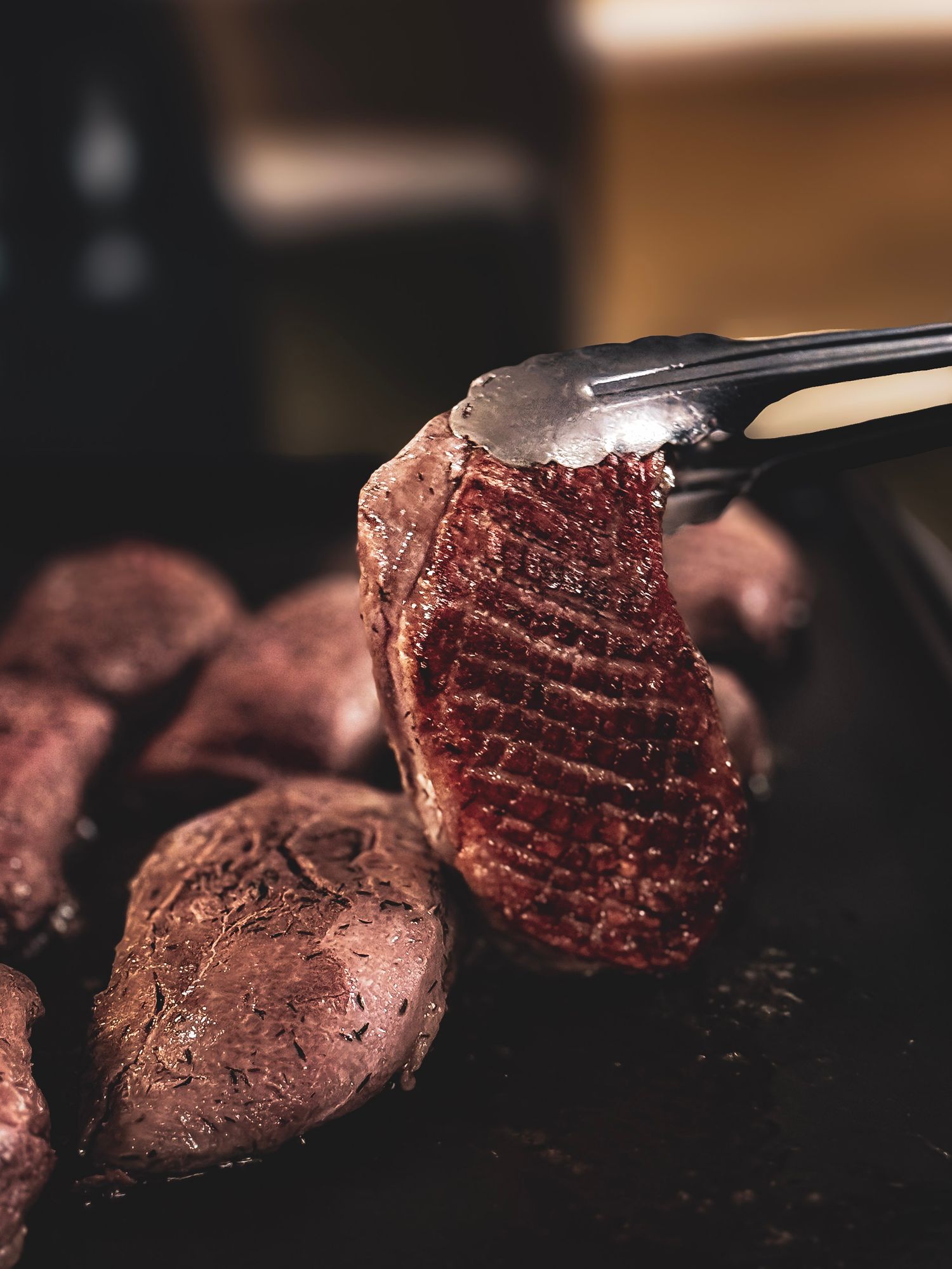 Grilled meat being lifted with tongs showing juicy medium-rare doneness.
