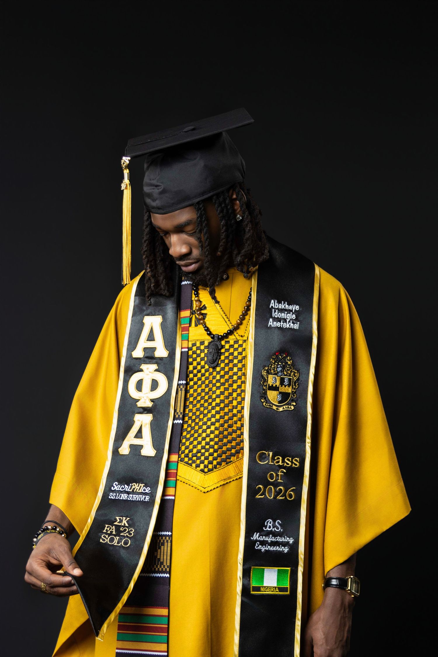 Graduate in yellow regalia and cap wearing Alpha Phi Alpha stole, Class of 2026 B.S. Manufacturing Engineering sash.