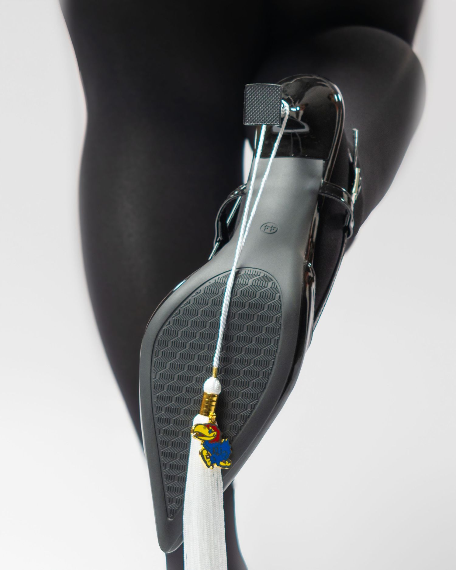 Black high heel shoe with University of Kansas Jayhawk charm tassel decoration on sole.