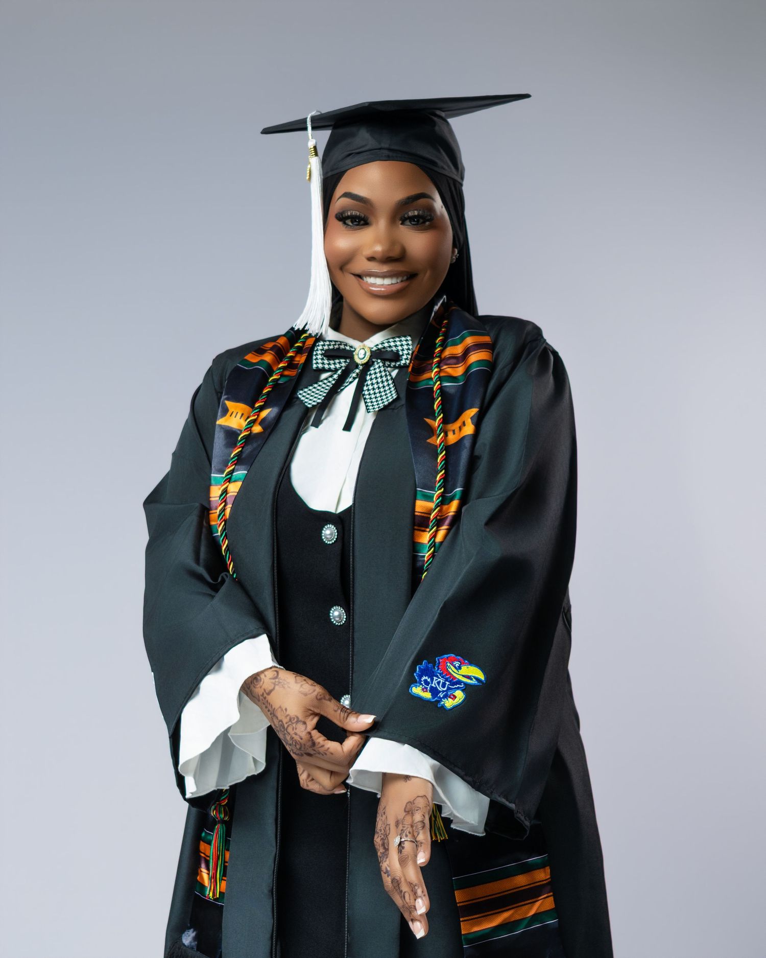 Graduate smiling in black cap and gown with colorful kente cloth stole at graduation portrait.