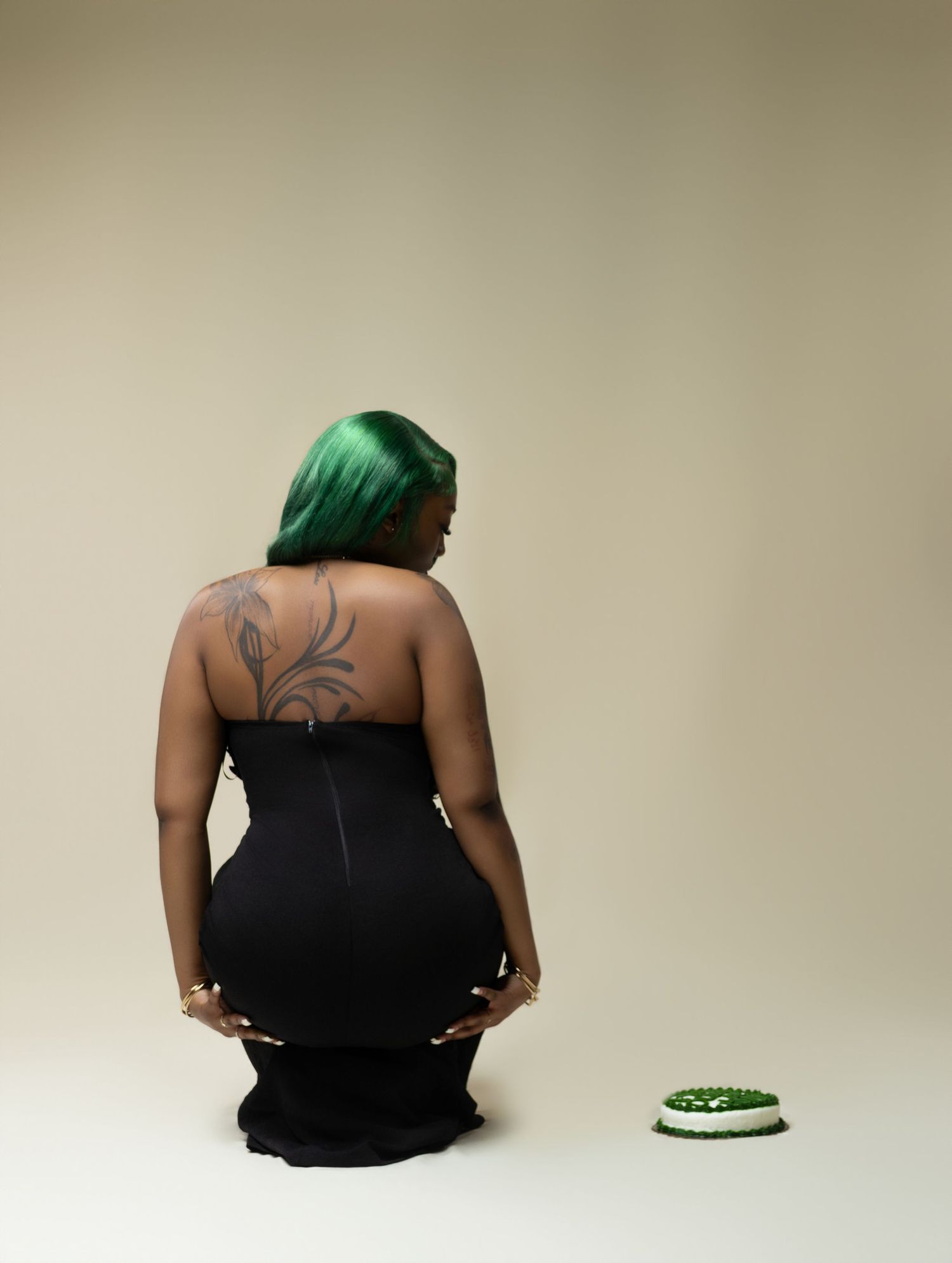 Woman with green hair in black strapless gown poses near small cake.