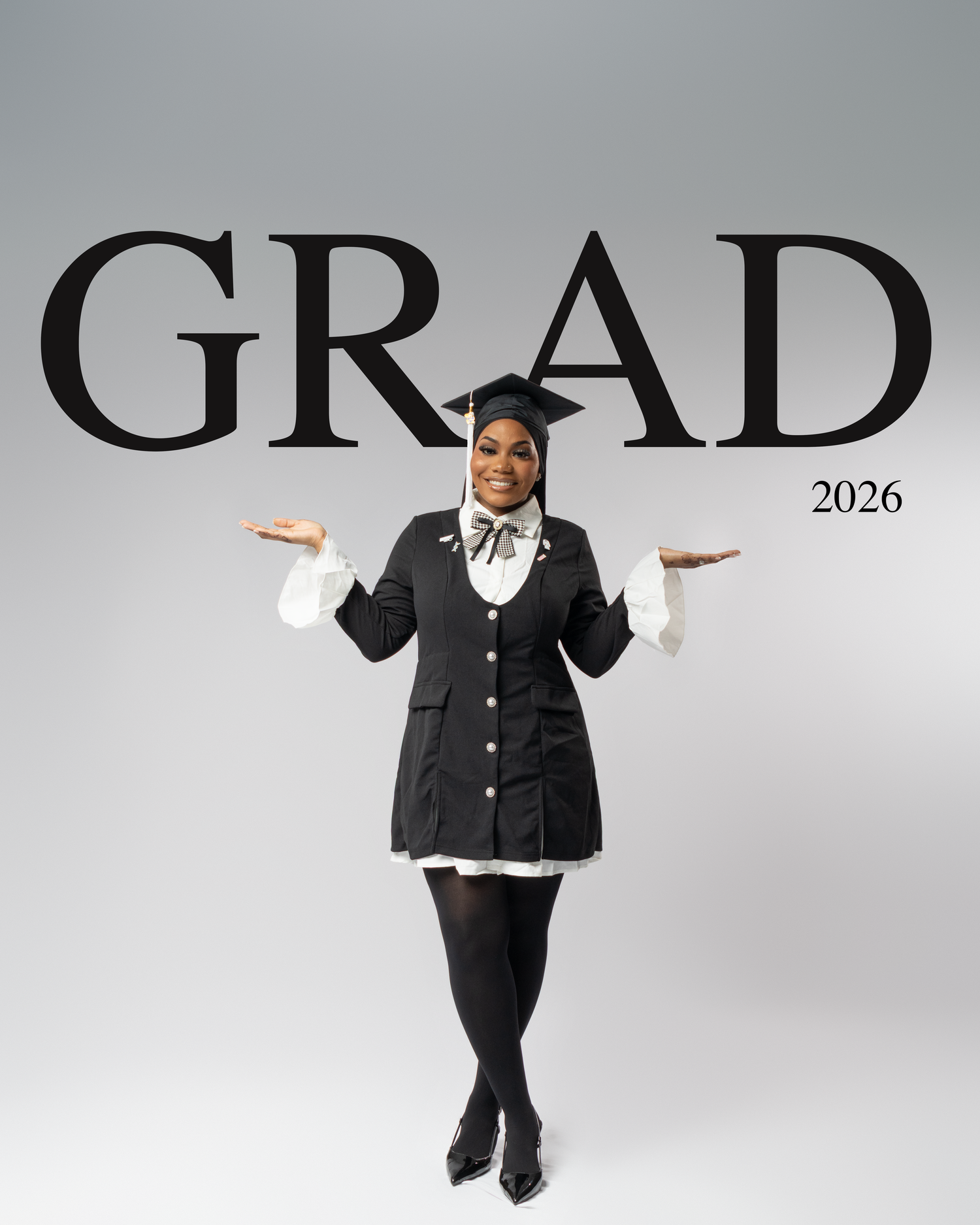 A smiling graduate in black cap and gown poses with open arms under bold GRAD 2026 text on gray background.