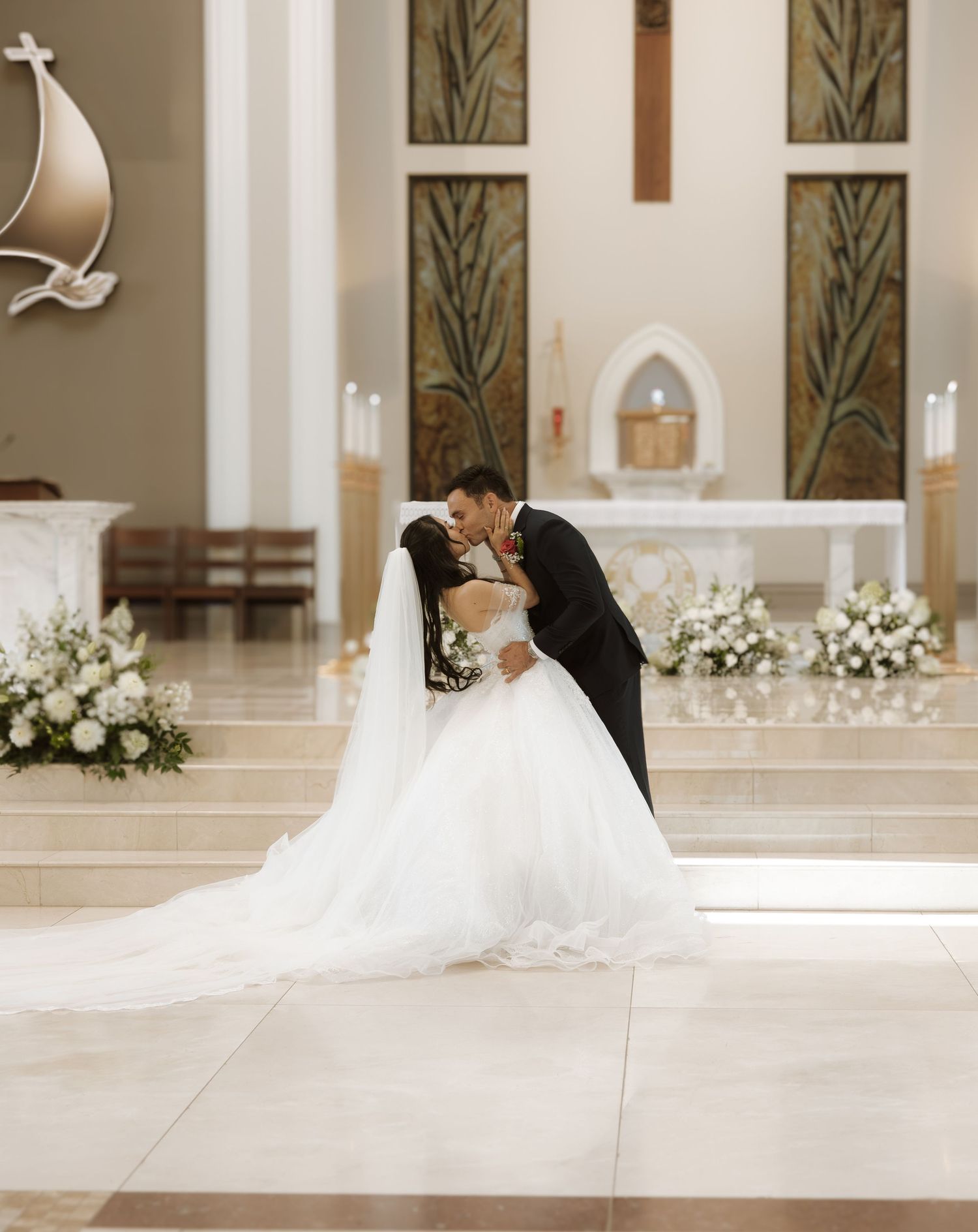 Interior of elegant church decorated with white flowers featuring stylish wedding couple on tiled floor during ceremony.