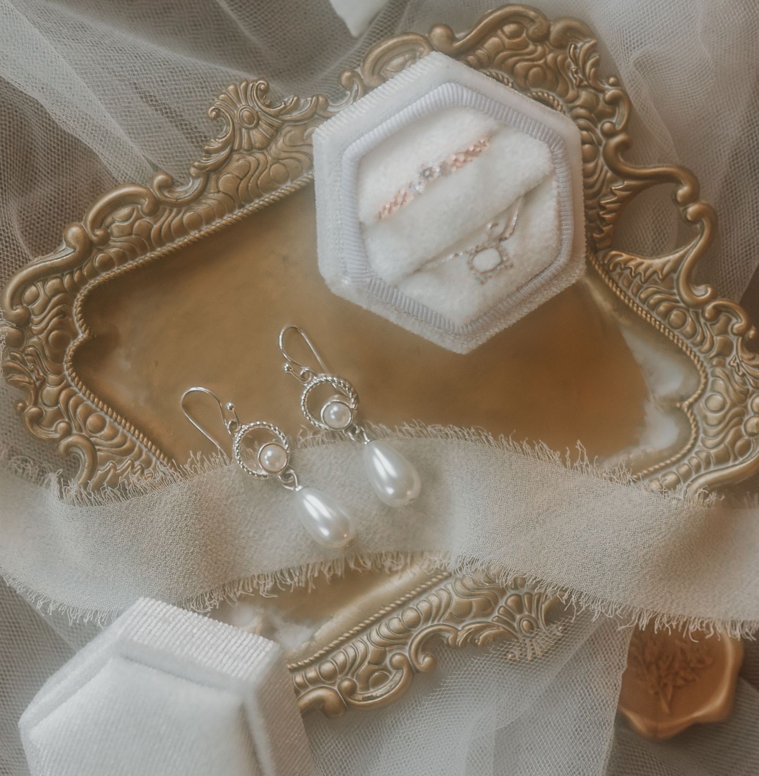 Wedding rings displayed in hexagonal box on ornate vintage tray with delicate fabric details.