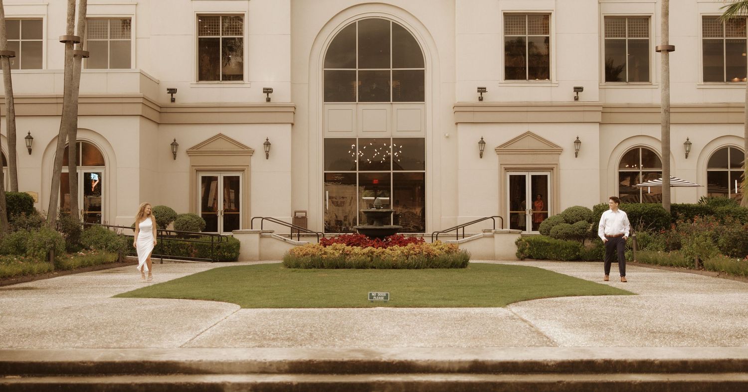 A panoramic view of a large white classical revival style building with columns, arches and landscaped grounds.