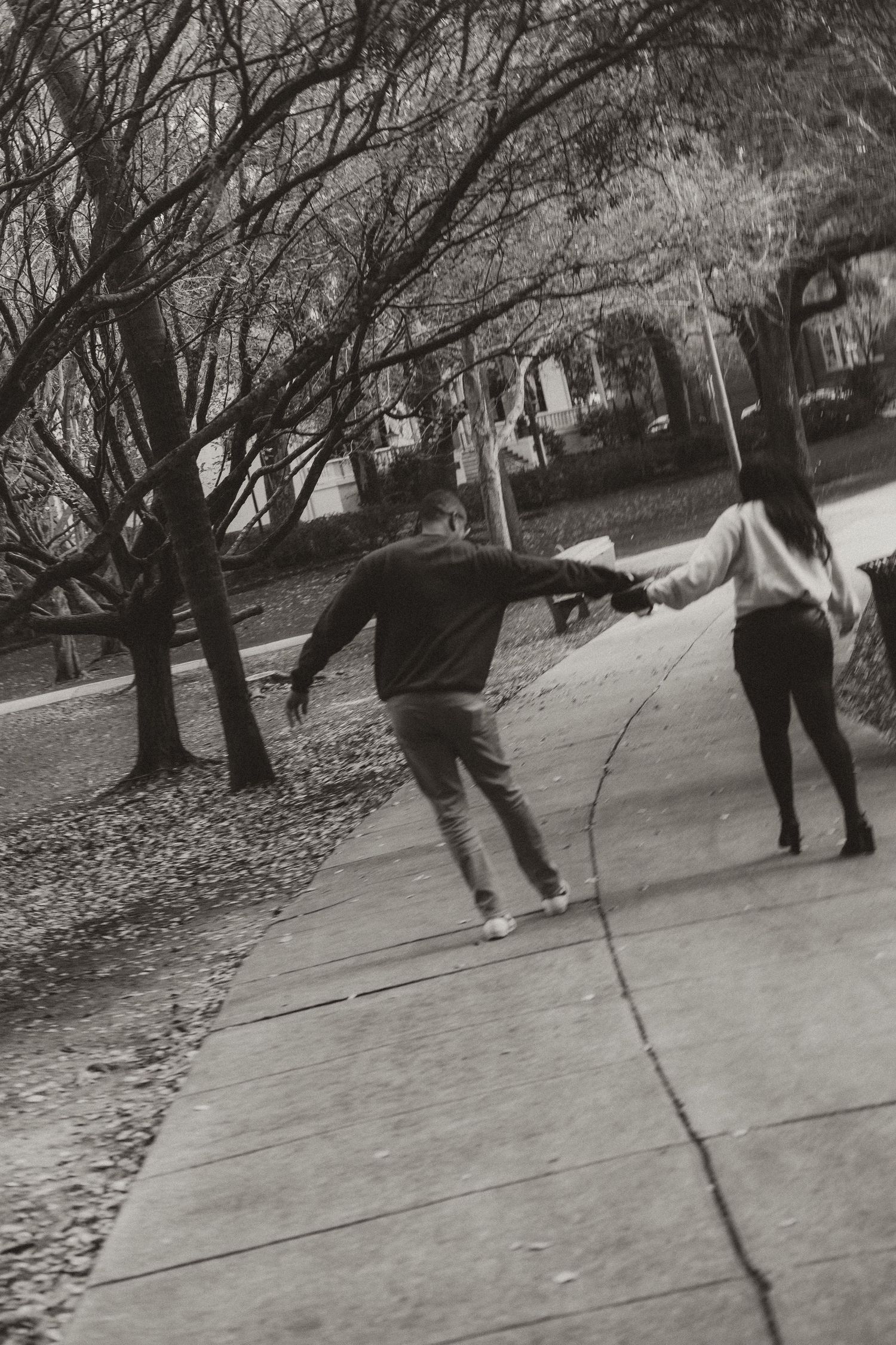 Black and white photo of couple holding hands while walking down a tree-lined path.