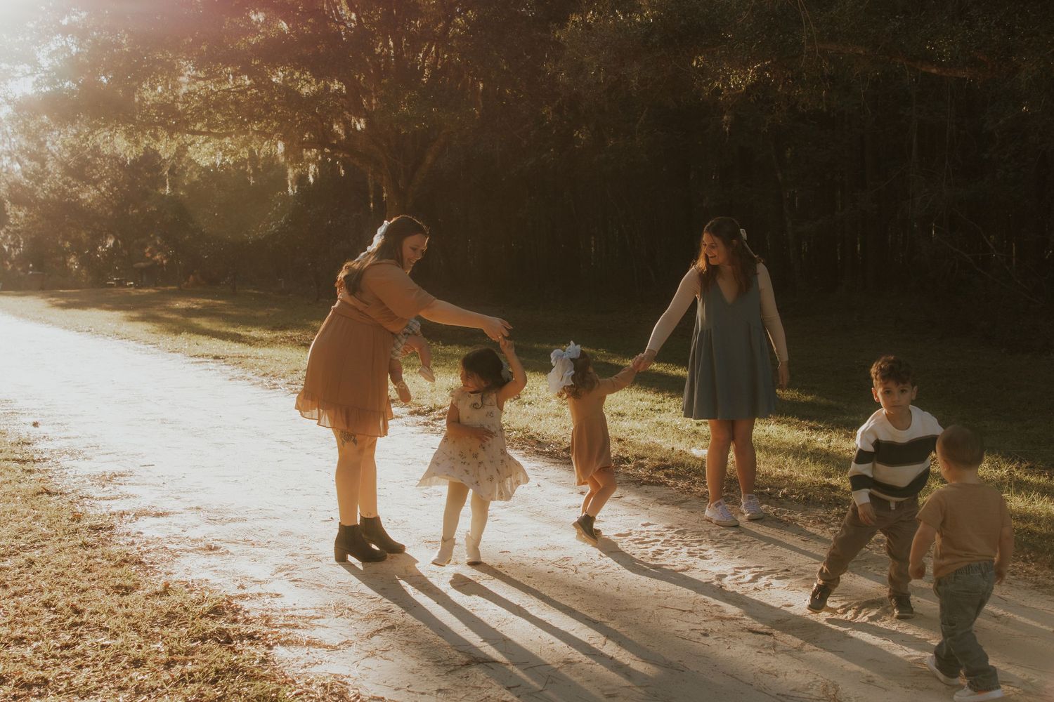 A family holds hands while walking together on a sunlit path.