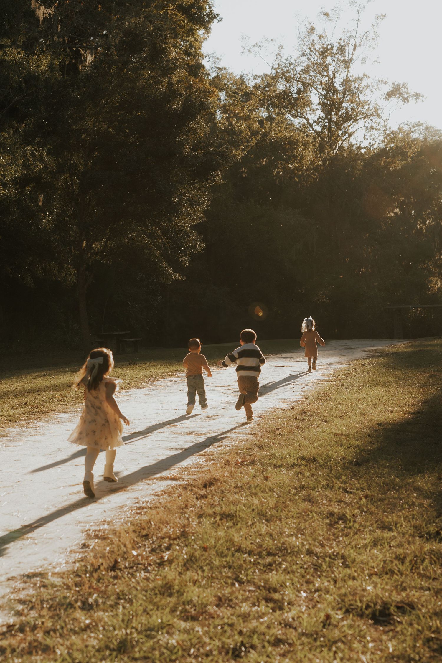Children running along a sunlit path through a park at golden hour.