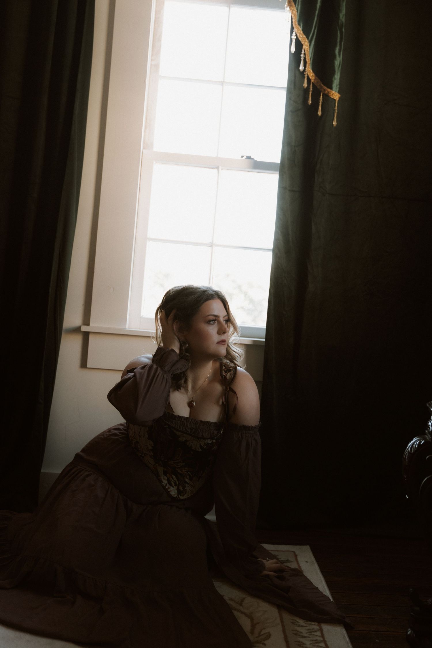 A silhouetted figure sits near a window in a dimly lit room creating a moody atmospheric scene.