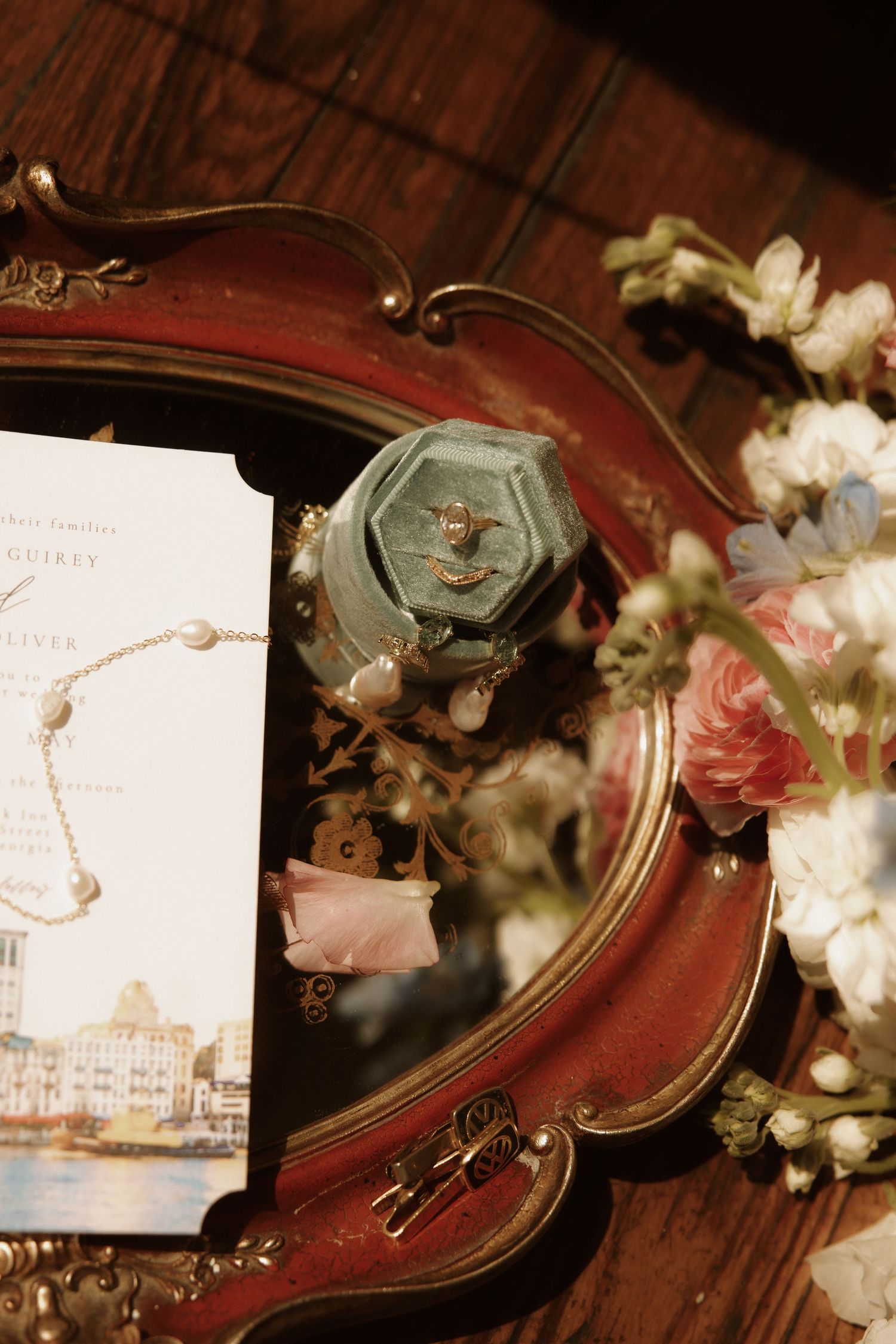 Vintage red vanity tray with velvet ring box, pearl bracelet, floral arrangement, and elegant wedding invitation.