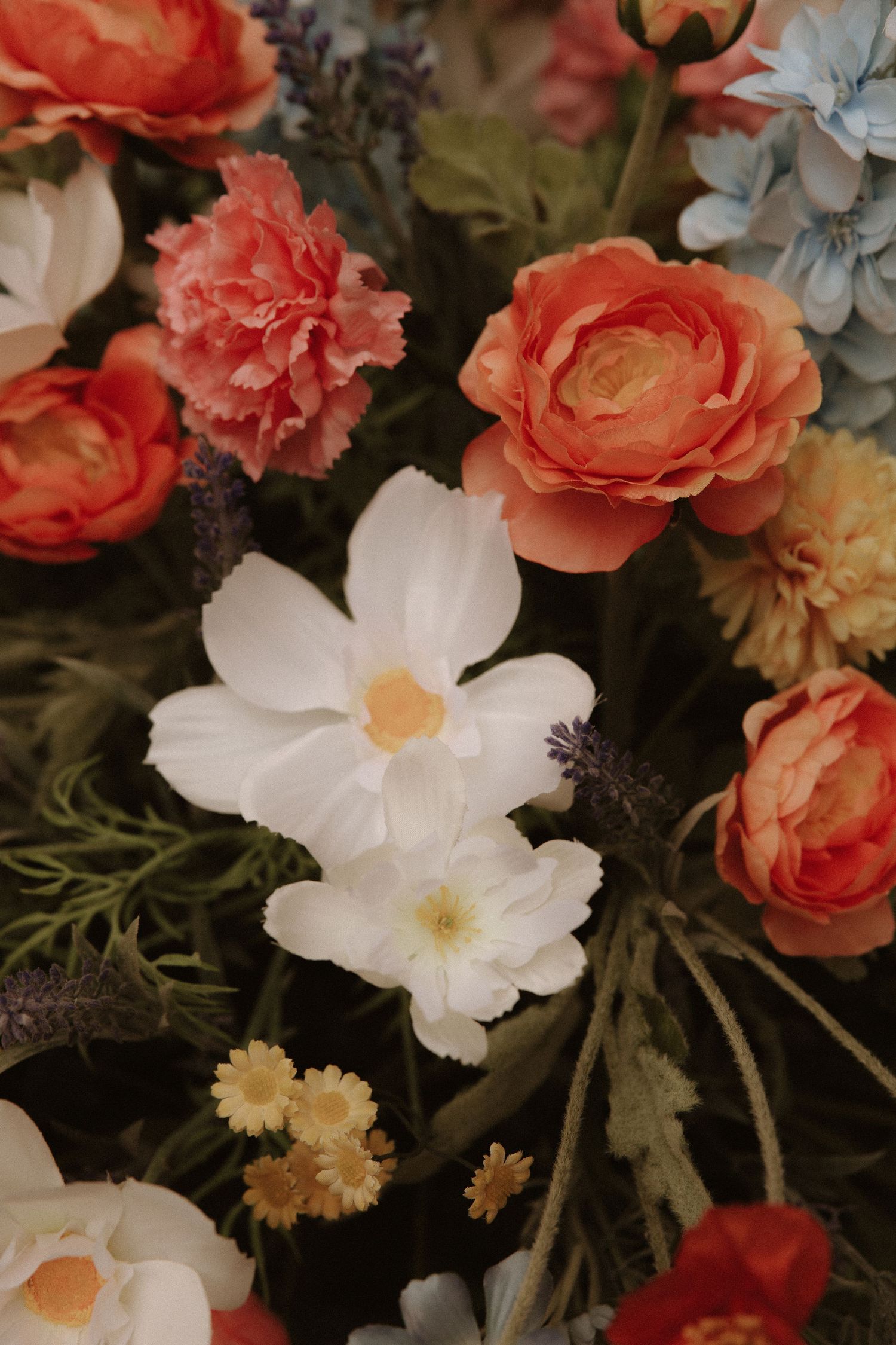 A romantic floral arrangement featuring coral roses, white cosmos flowers, and pale yellow blooms against dark foliage.