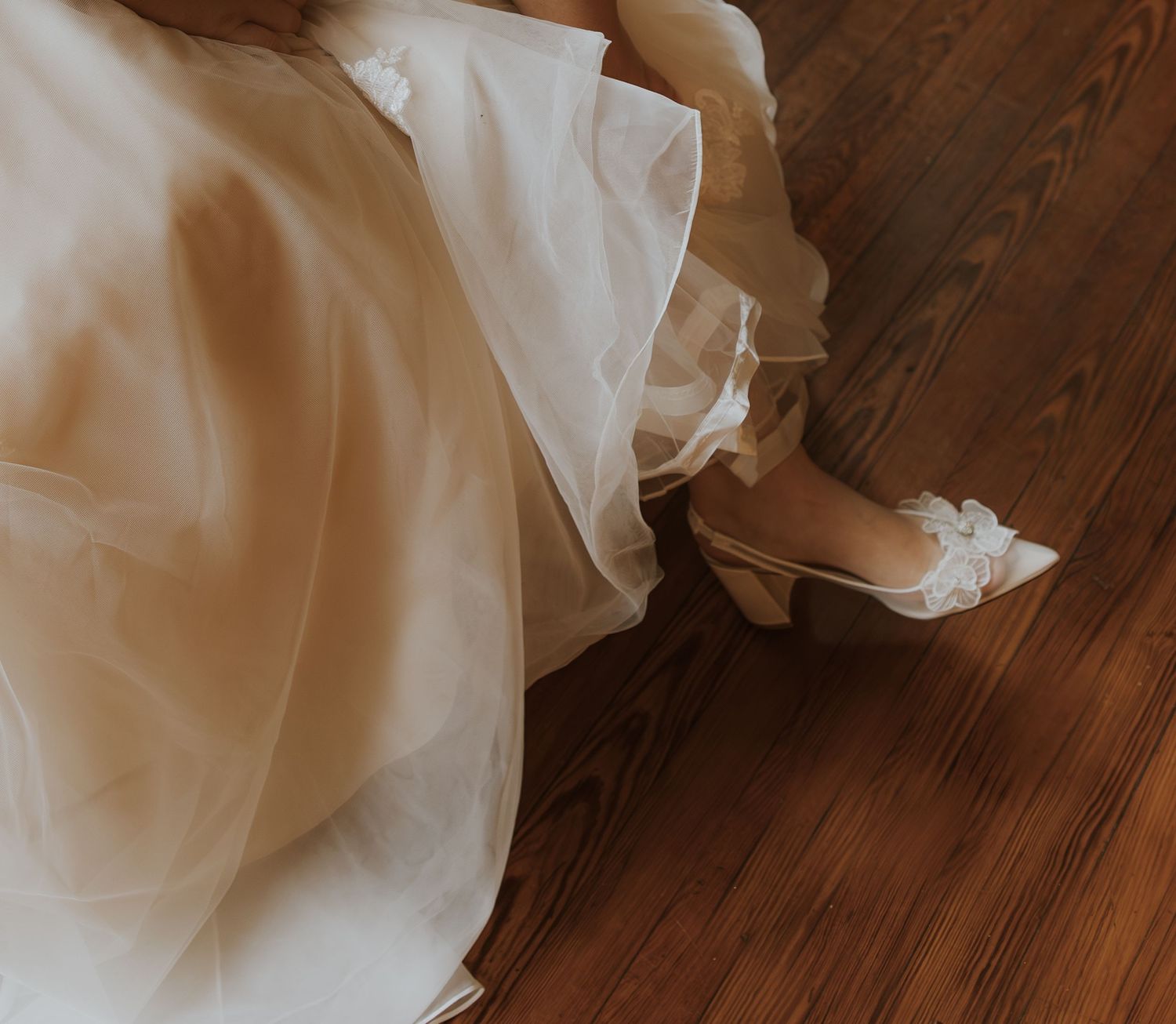 White wedding dress and shoes on a polished hardwood floor.