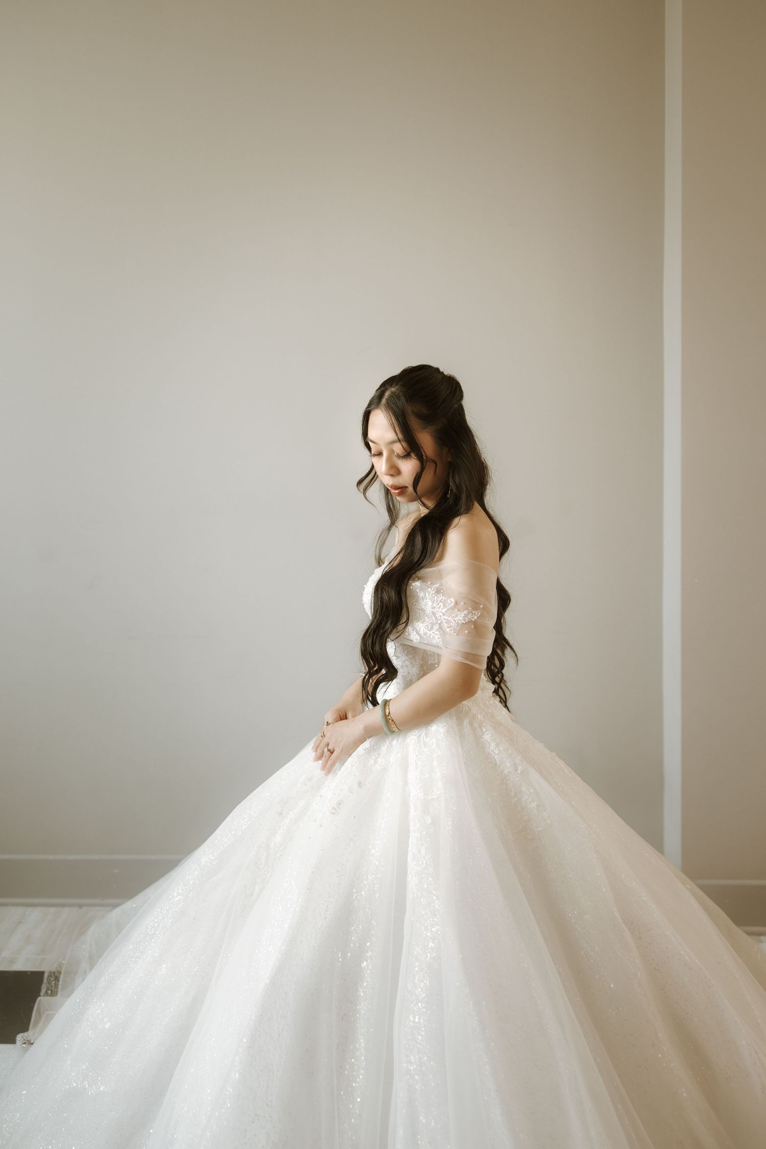 A bride in a magnificent white ball gown poses gracefully against a neutral wall showing the elegant flow of her dress.