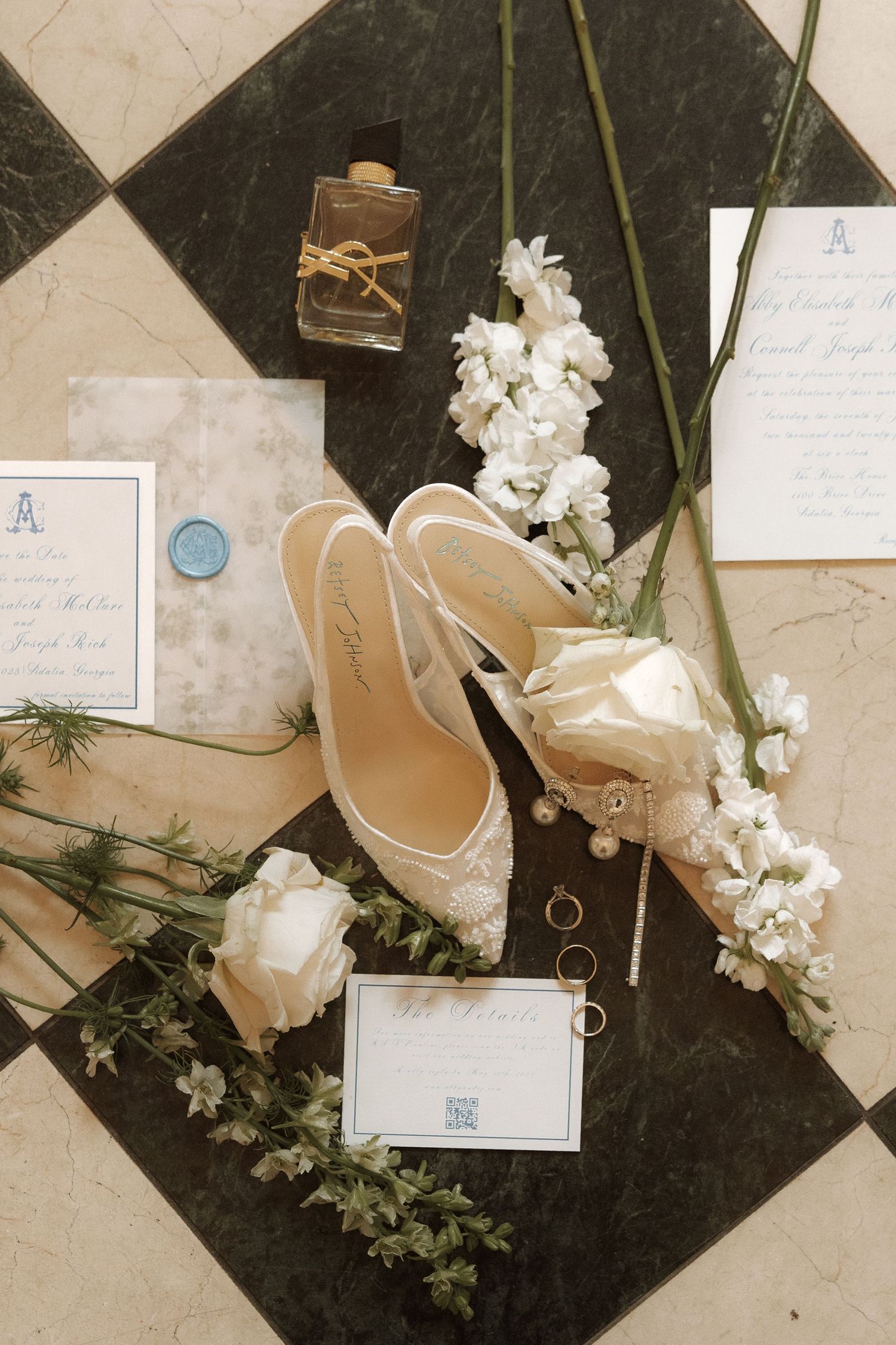 Elegant white wedding shoes arranged with delicate white flowers and handwritten notes on a black and white checkered floor.