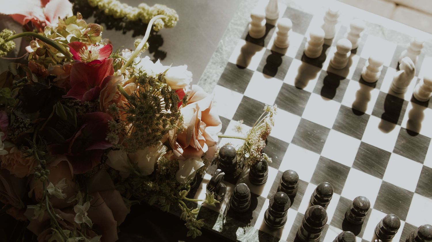 Vintage glass chess pieces arranged on a checkered board next to floral arrangements.